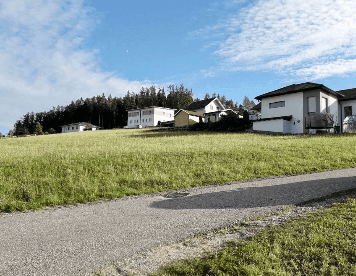 Sonnige Landschaft mit Wohnhäusern, grüner Wiese und einem Weg unter klarem Himmel.