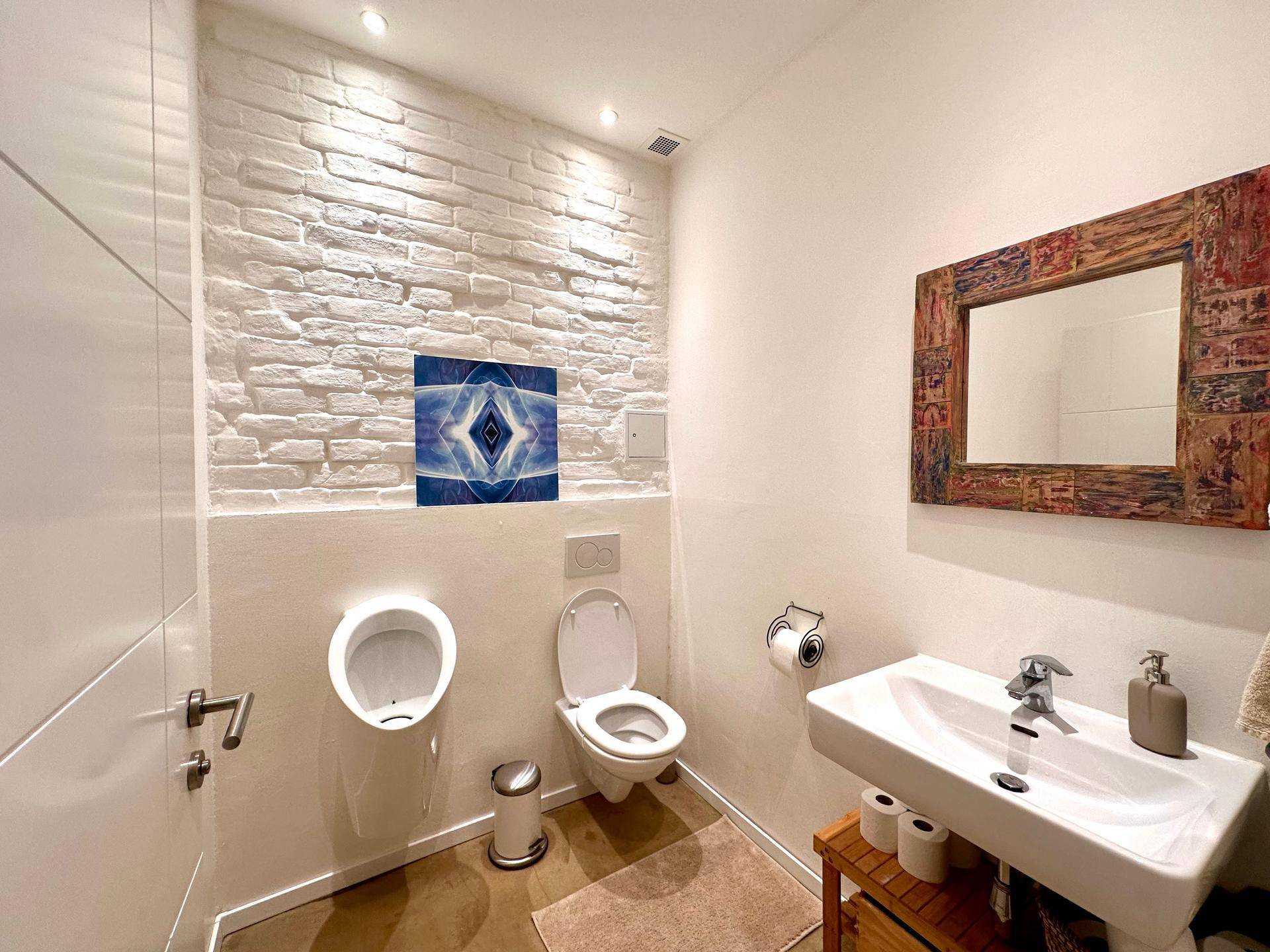 Modernes Gäste-WC mit Urinal, wandhängendem WC und Waschbecken, akzentuiert durch eine Ziegelwand.