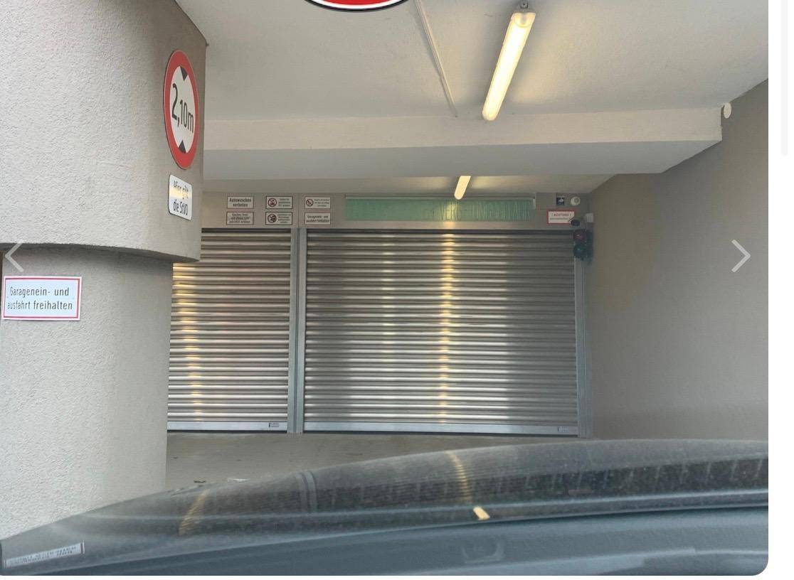 Einfahrt zu einer Tiefgarage mit zwei geschlossenen Rolltoren und Höhenbegrenzungsschild.