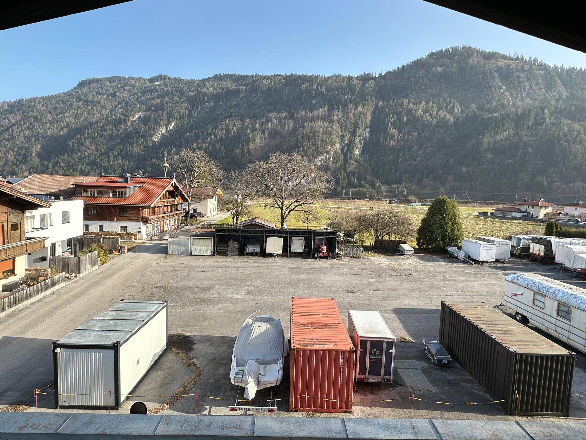 Weitläufiges Außengelände mit Lagercontainern und einem Boot, umgeben von einer beeindruckenden Berglandschaft.