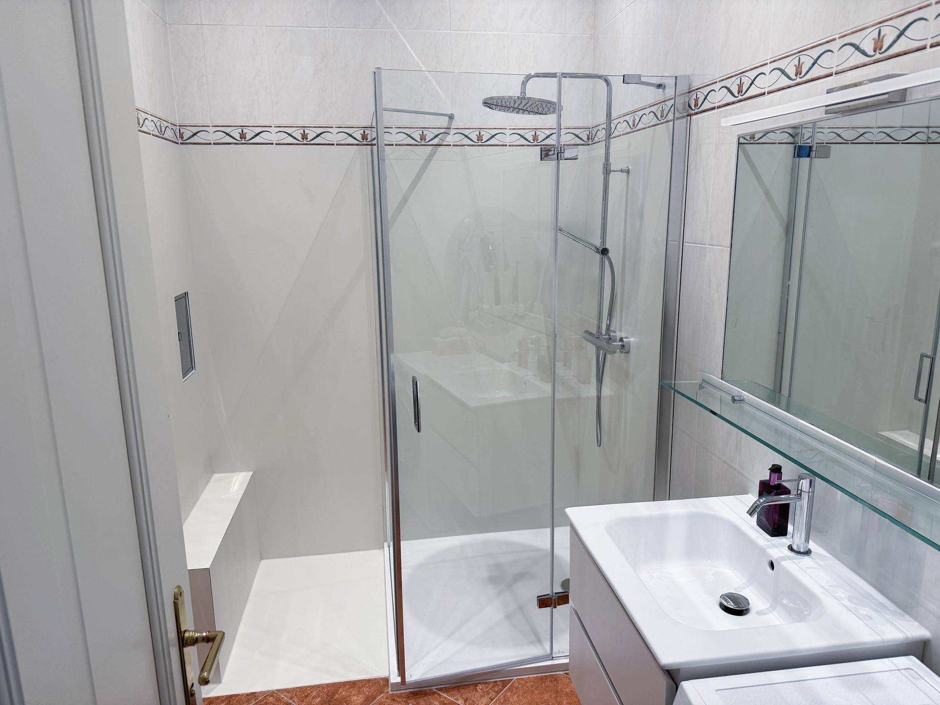 Modernes Badezimmer mit Glasduschkabine, Regendusche und Einzelwaschbecken auf Marmorplatte.