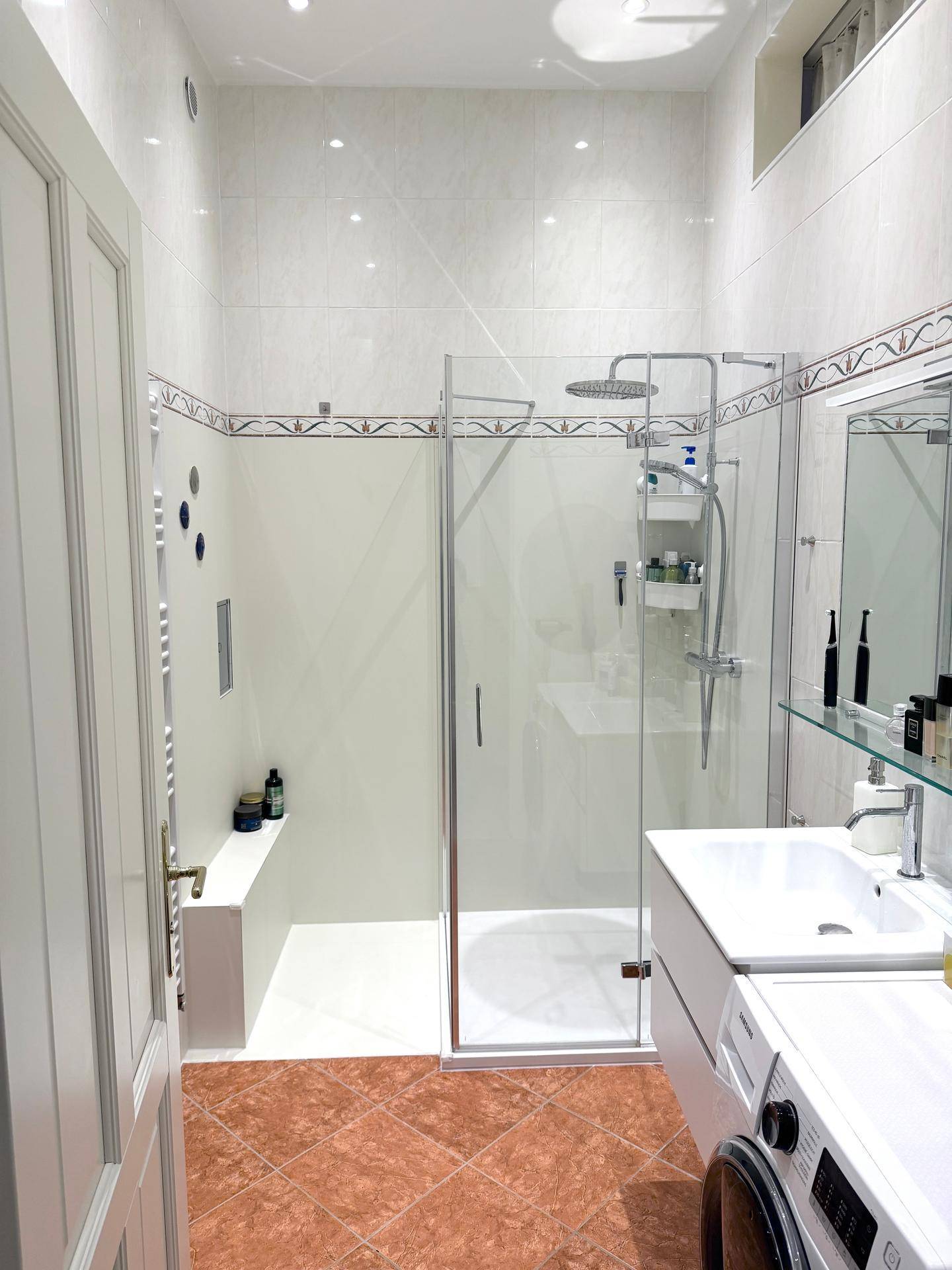 Modernes Badezimmer mit Duschkabine, Waschbecken und Terrakotta-Fliesenboden, ausgestattet mit einer Waschmaschine.