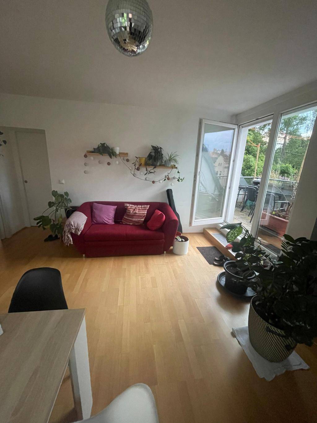 Helles Wohnzimmer mit Holzboden, rotem Sofa und Zugang zur Dachterrasse.