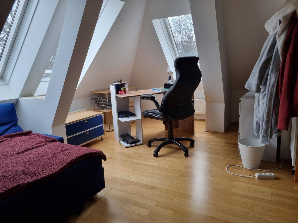 Arbeitsbereich im Dachzimmer mit Schreibtisch, Bürostuhl und Blick durch die Dachfenster.