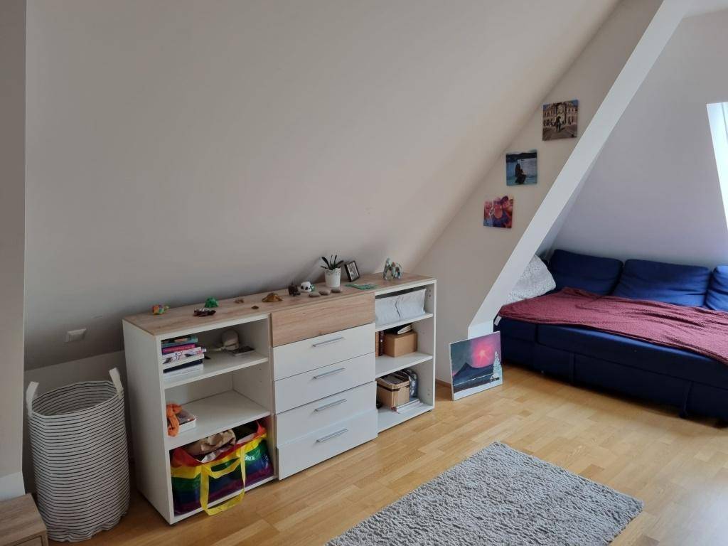 Dachzimmer mit praktischen Aufbewahrungsmöbeln, blauer Couch und Holzboden.