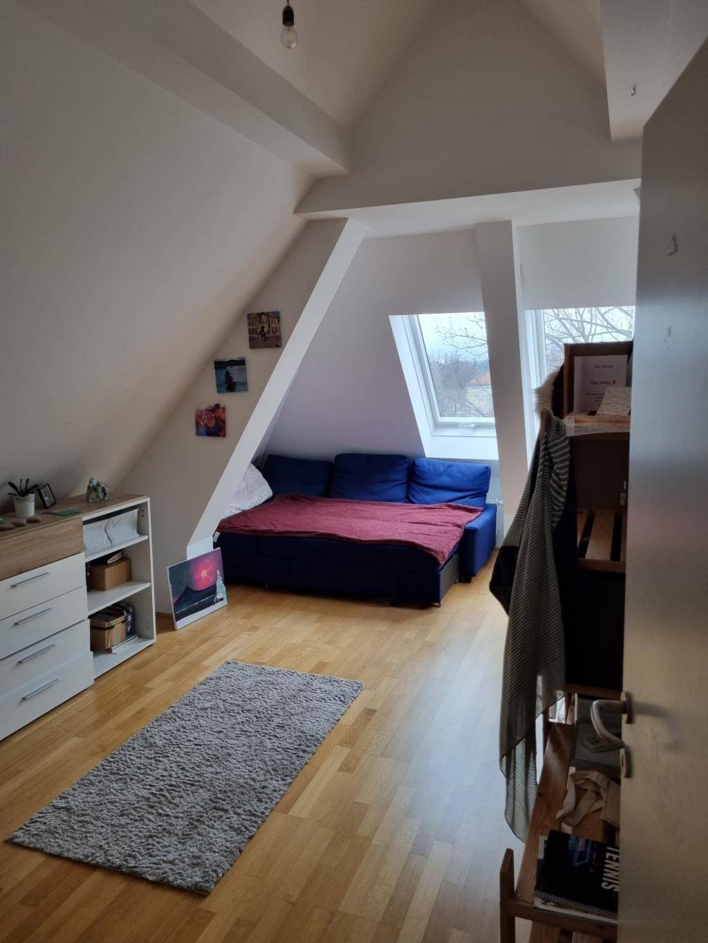 Gemütliches Dachzimmer mit Holzboden, blauer Couch und schrägen Wänden, ideal als Schlaf- oder Wohnbereich.