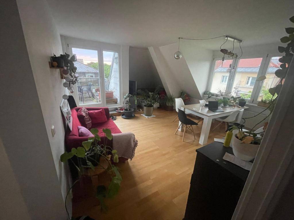 Offener Wohn-Essbereich mit Holzboden, rotem Sofa und großen Fenstern zur Terrasse.