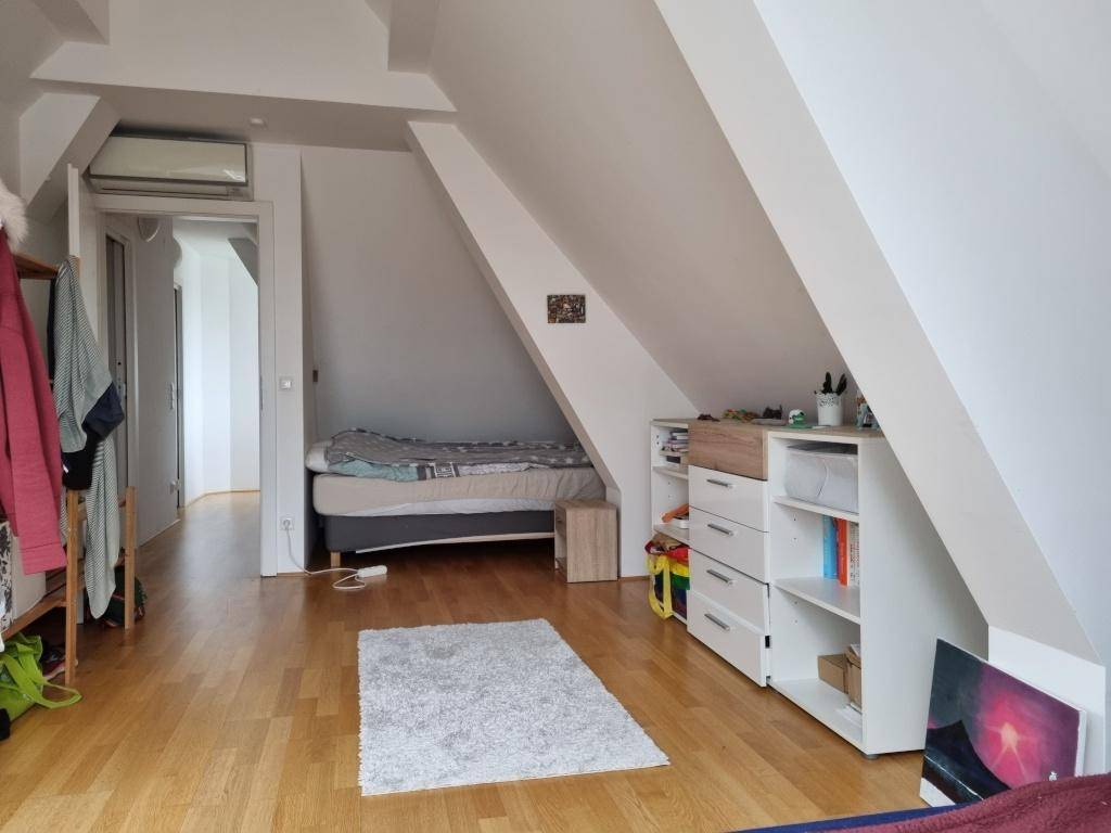 Geräumiges Dachzimmer mit zweitem Bett, Holzboden und Zugang zu einem weiteren Raum.