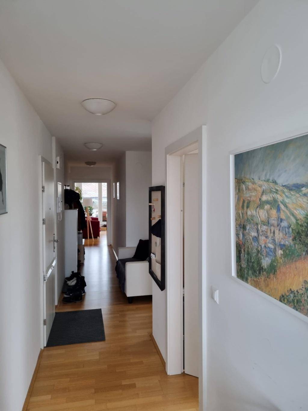 Heller Flur mit Holzboden und Kunst an den Wänden, der zu den Wohnbereichen führt.