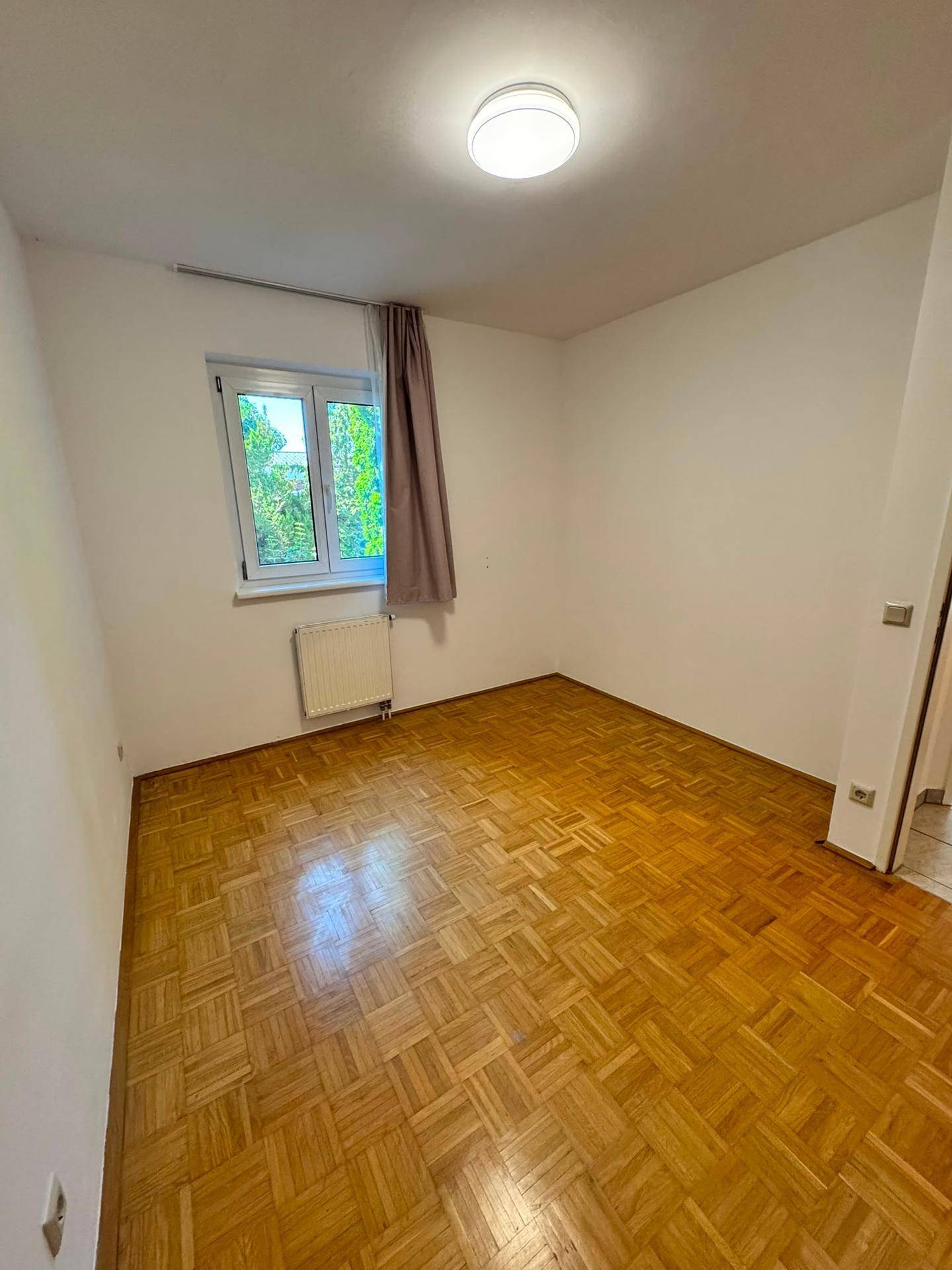 Schlichtes Schlafzimmer mit Parkettboden und Fenster mit Grünblick.