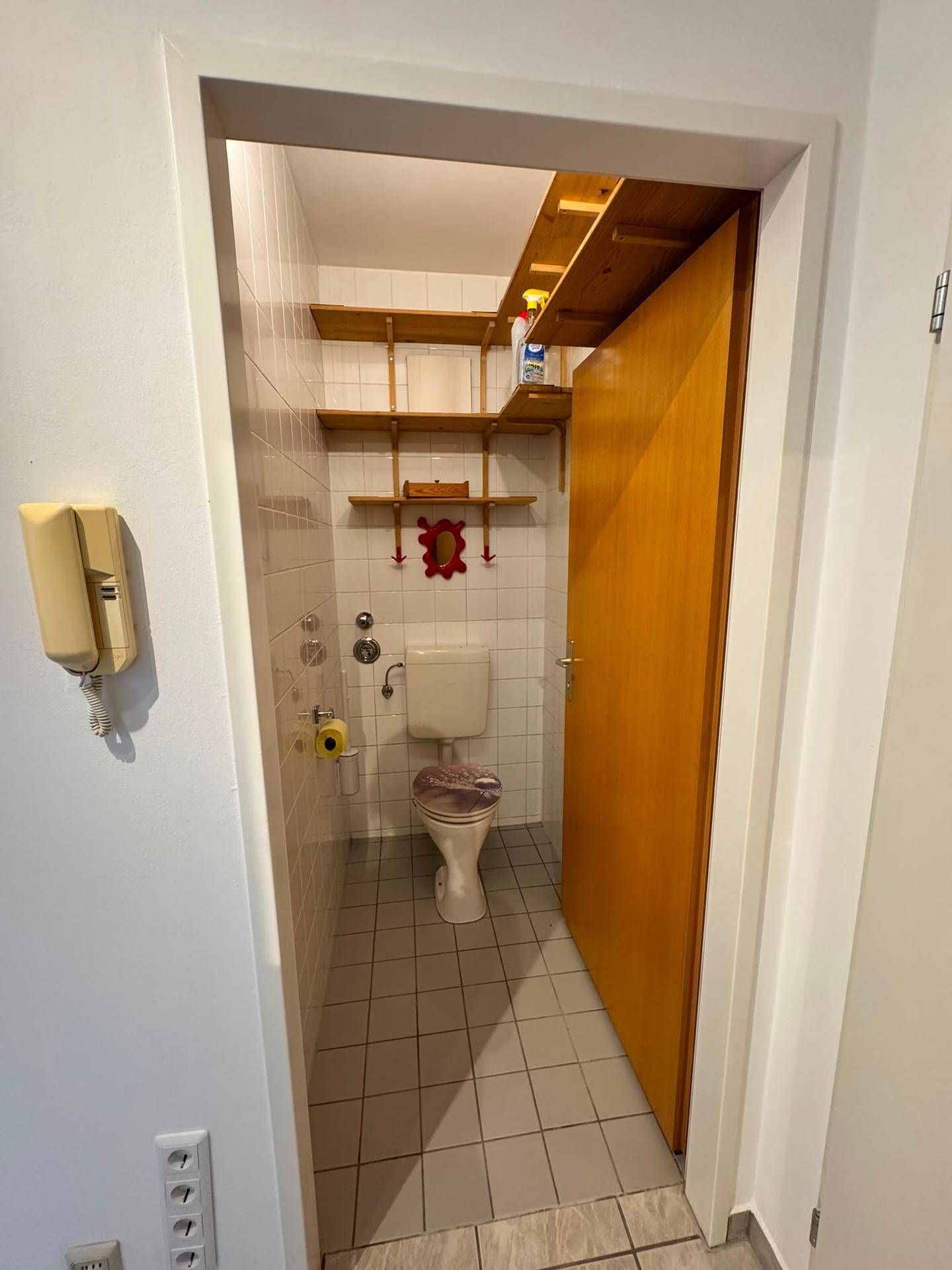 Kleines Gäste-WC mit Toilette, Waschbecken und Wandregalen.