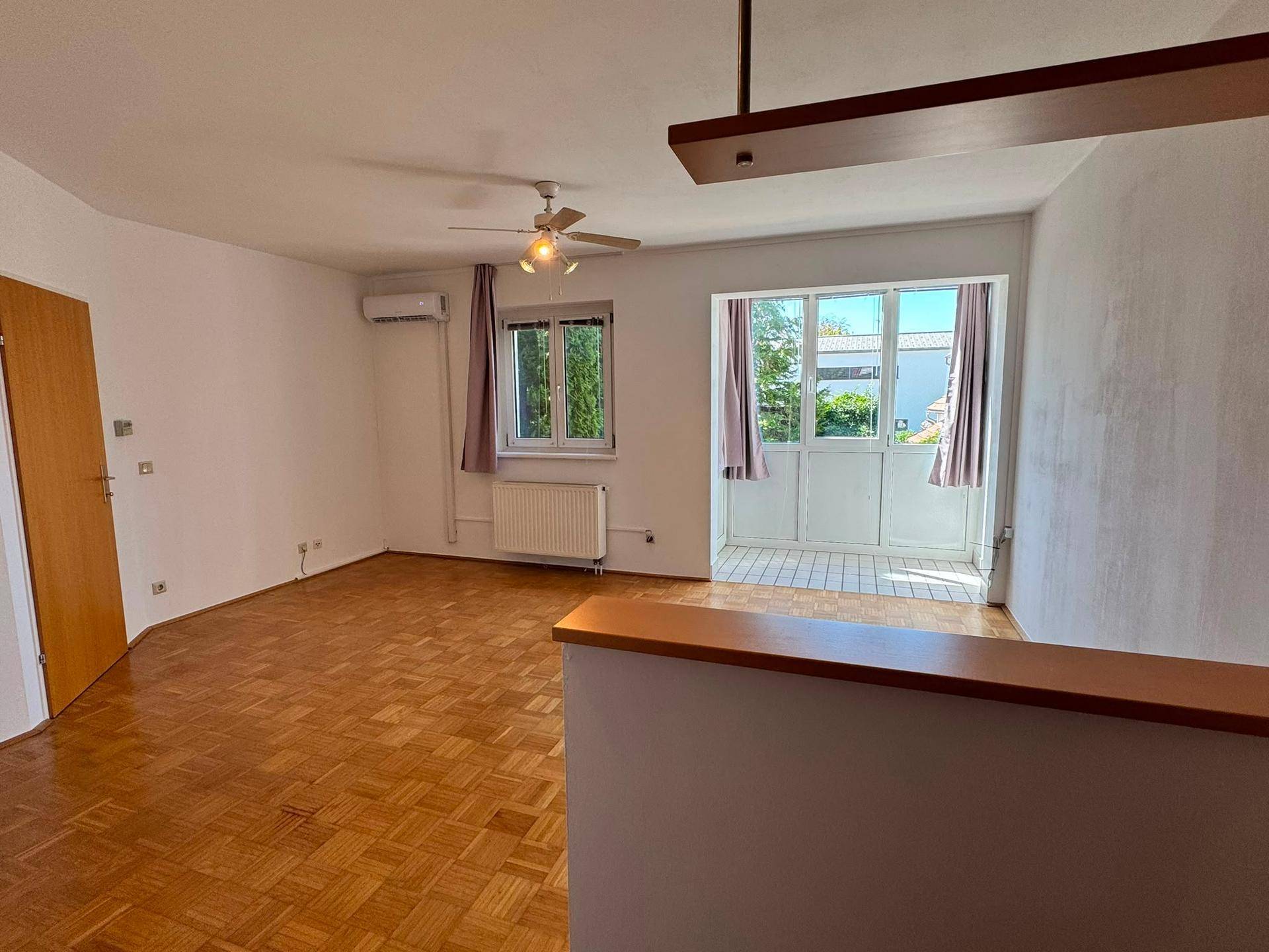 Helles Wohnzimmer mit Parkettboden, Klimaanlage und Zugang zum Balkon.