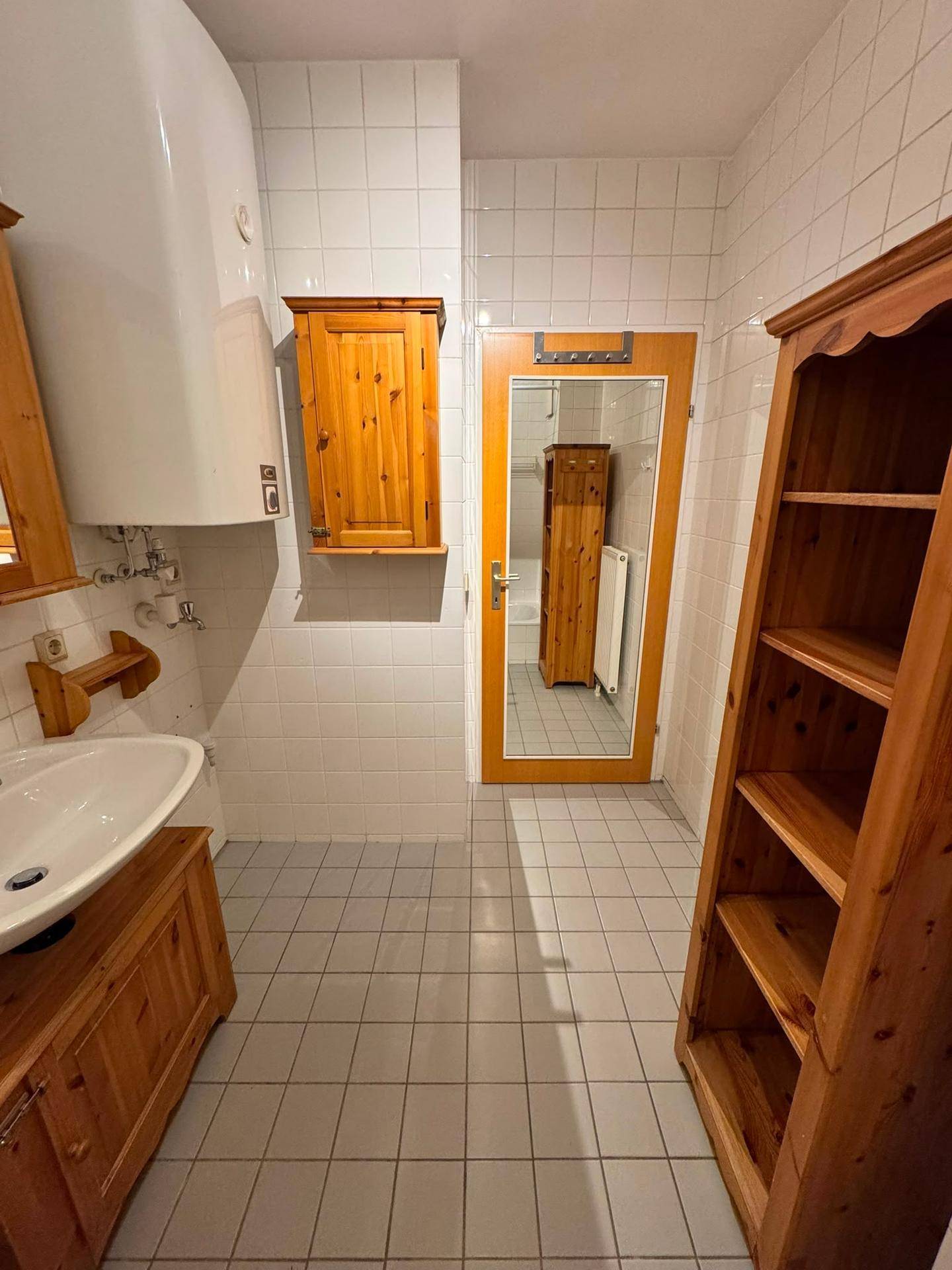 Gefliestes Badezimmer mit Holzschränken und Boiler an der Wand.