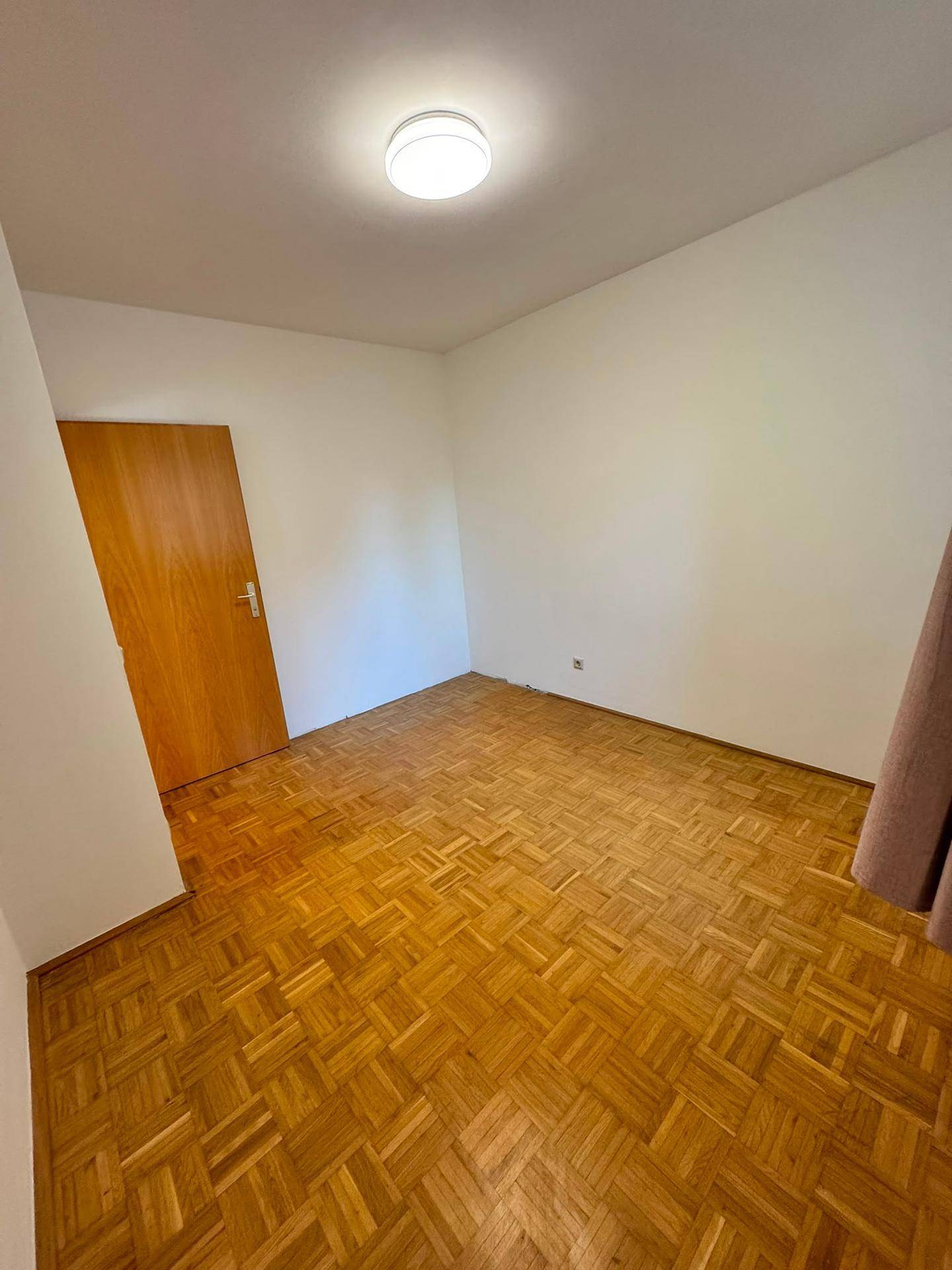 Leeres Schlafzimmer mit Parkettboden und einfacher Beleuchtung.
