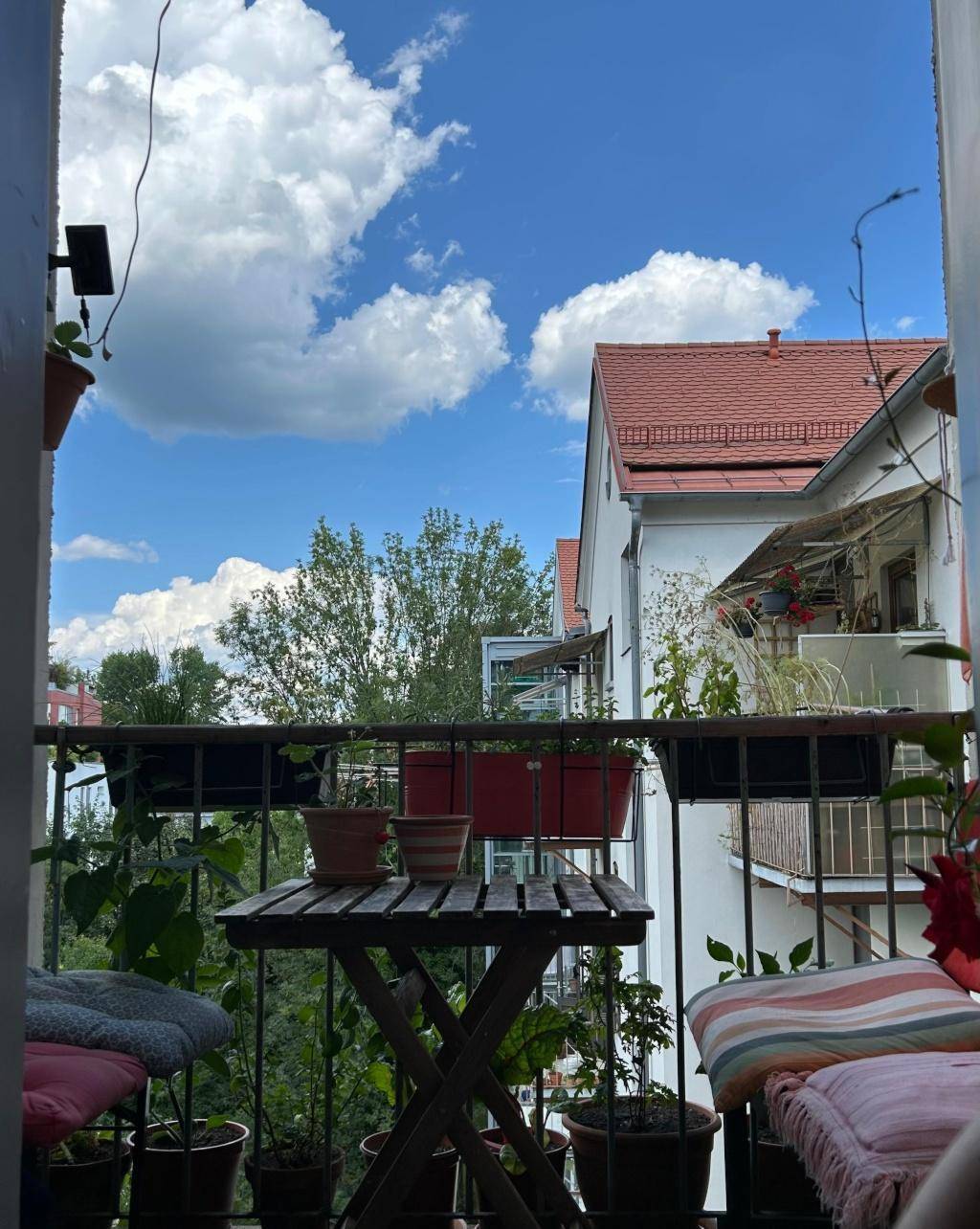 Gemütlicher Balkon mit Pflanzen, kleinem Tisch und Blick auf umliegende Gebäude.