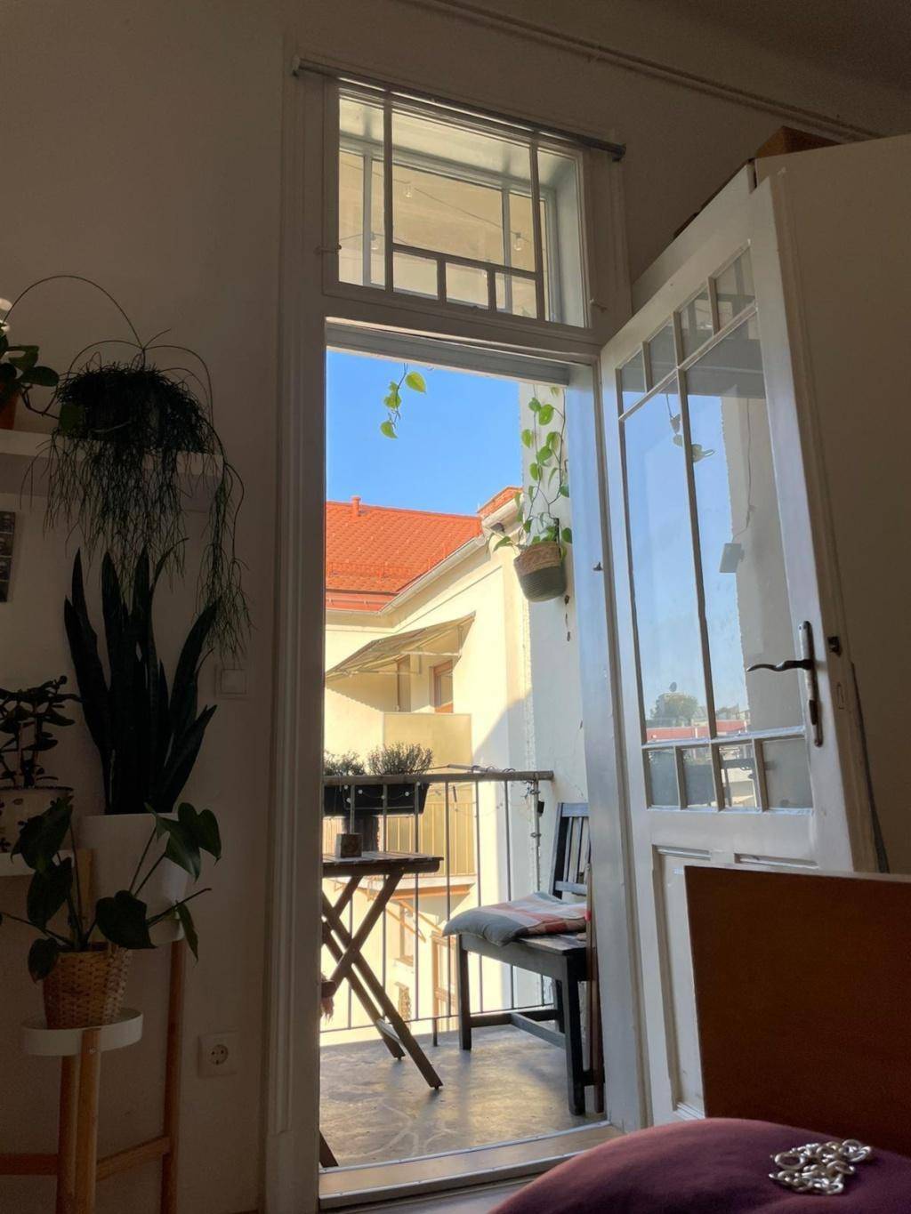 Heller Balkon mit kleinem Tisch und Stühlen, zugänglich durch eine Glastür.
