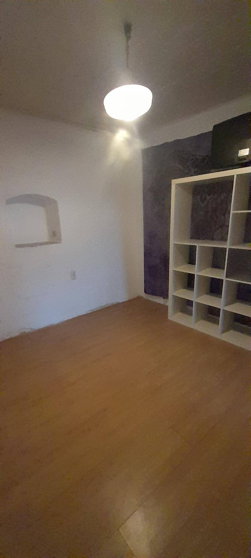 Leerer Raum mit Laminatboden und einem Regal an der Wand, bereit zur individuellen Gestaltung.