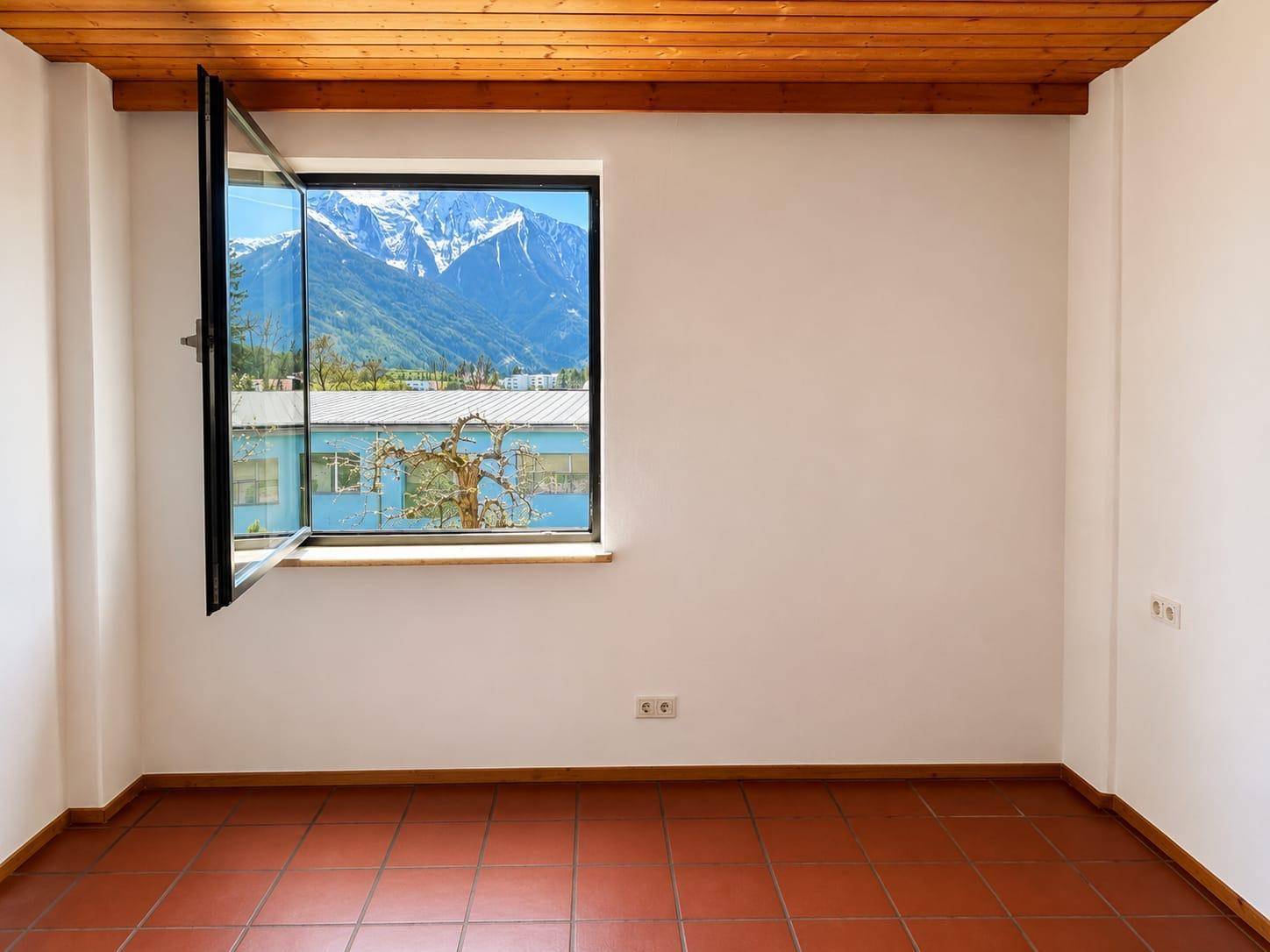 Heller Raum mit Terrakottafliesen, Holzdecke und weitem Bergblick durch das Fenster.