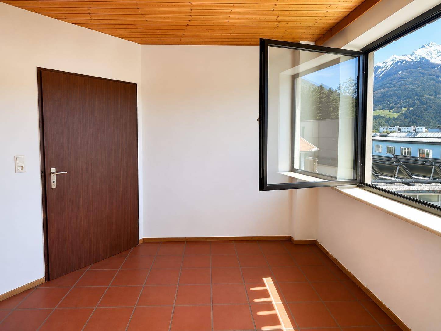 Leerer Raum mit Terrakottafliesen, Holzdecke und Fenster mit Bergblick.