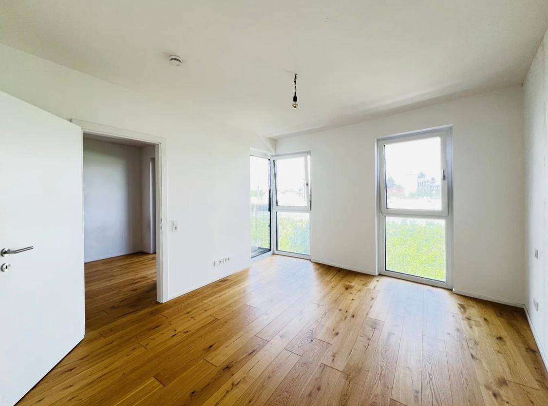 Helles Schlafzimmer mit Parkettboden und großen Fenstern für viel Tageslicht.