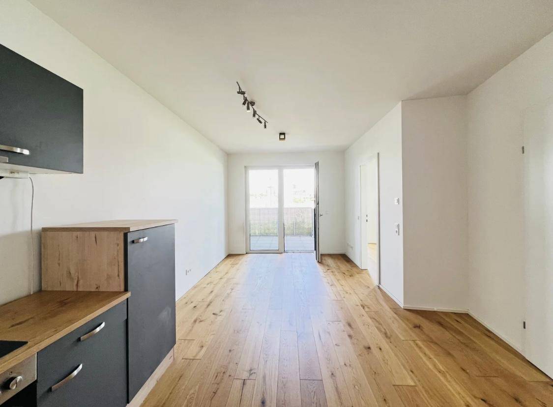 Lichtdurchfluteter Wohnbereich mit moderner Küchenzeile und Zugang zu einem Balkon.