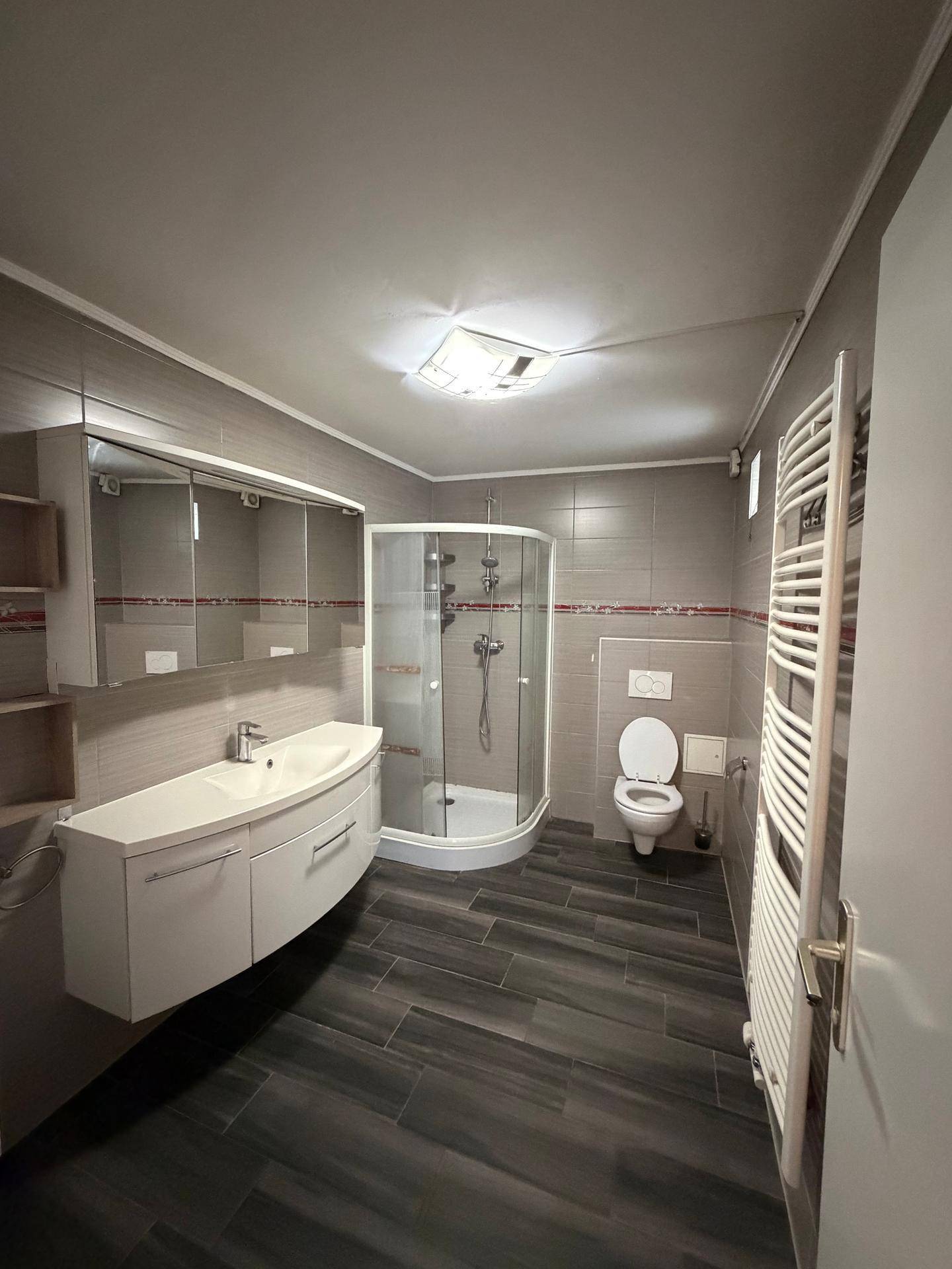 Modernes Badezimmer mit Duschkabine, schwebendem Waschtisch und Handtuchheizkörper.