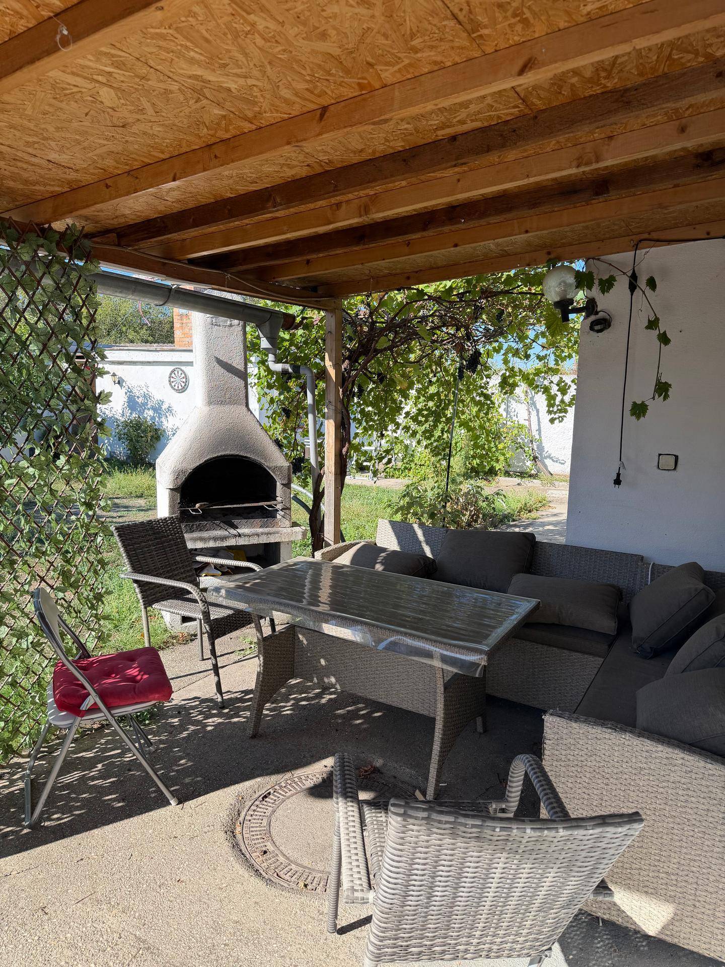 Überdachte Terrasse mit Gartenmöbeln und gemauertem Grillbereich im Freien.