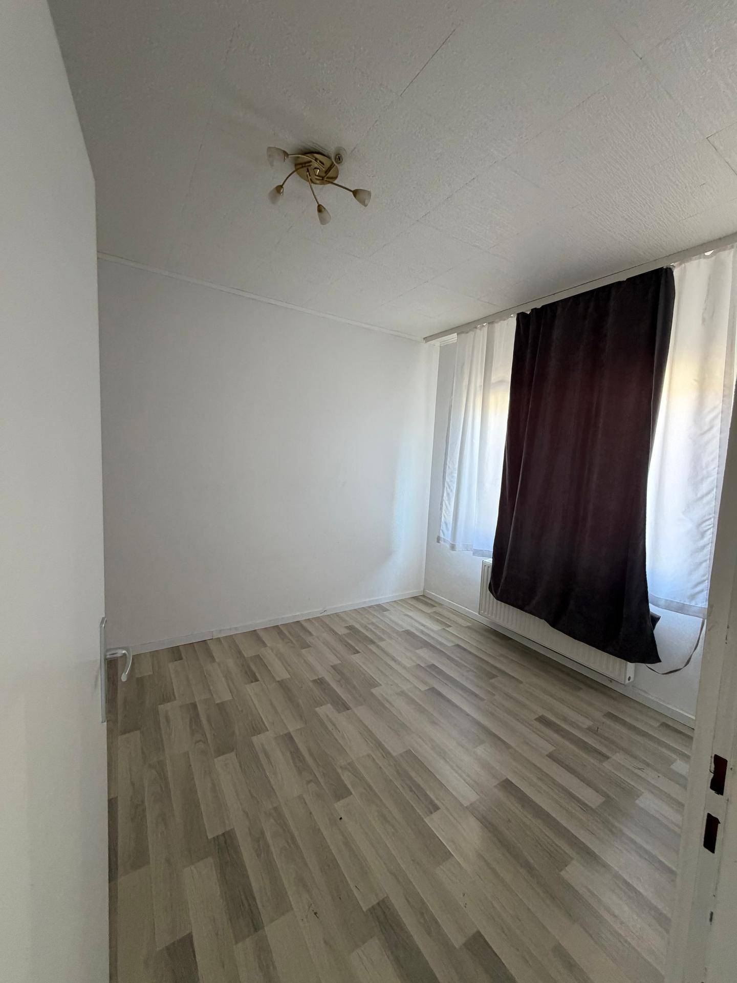 Helles Schlafzimmer mit modernem Laminatboden und Fenster mit dunklem Vorhang.