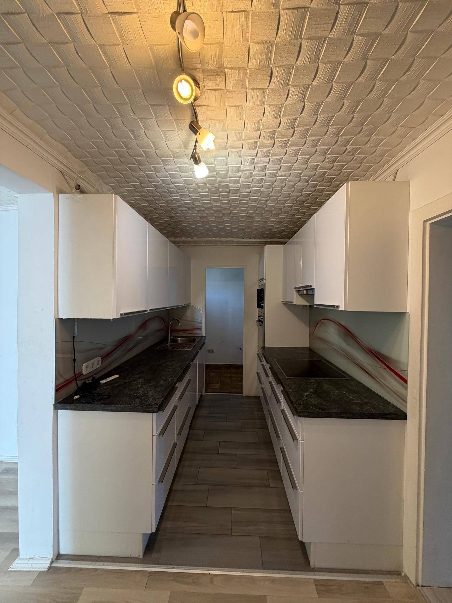Funktionale Küche mit weißen Schränken, dunklen Arbeitsplatten und Deckenbeleuchtung.