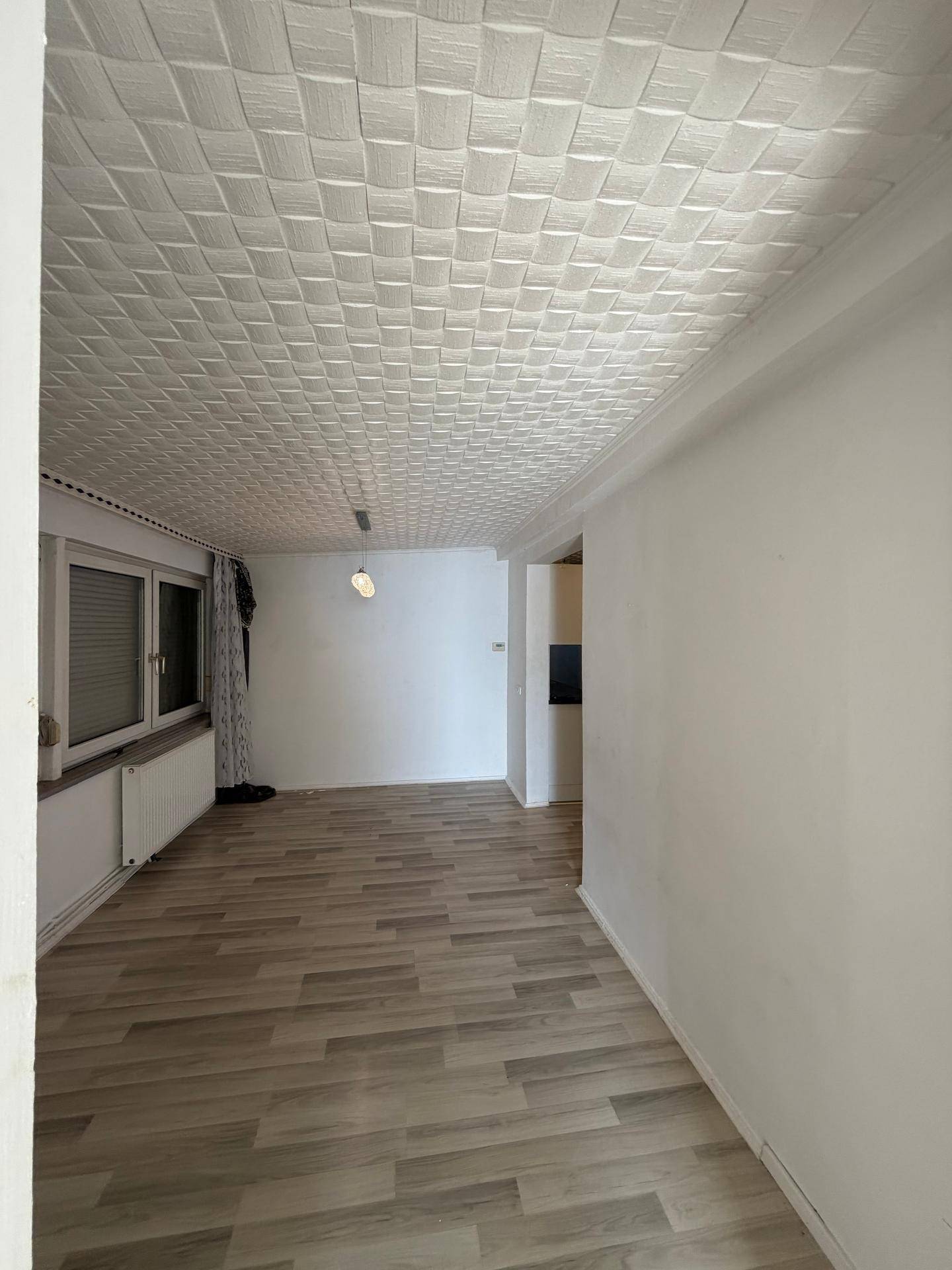 Heller Wohnbereich mit Laminatboden, weißen Wänden und Fenster mit Rollläden.