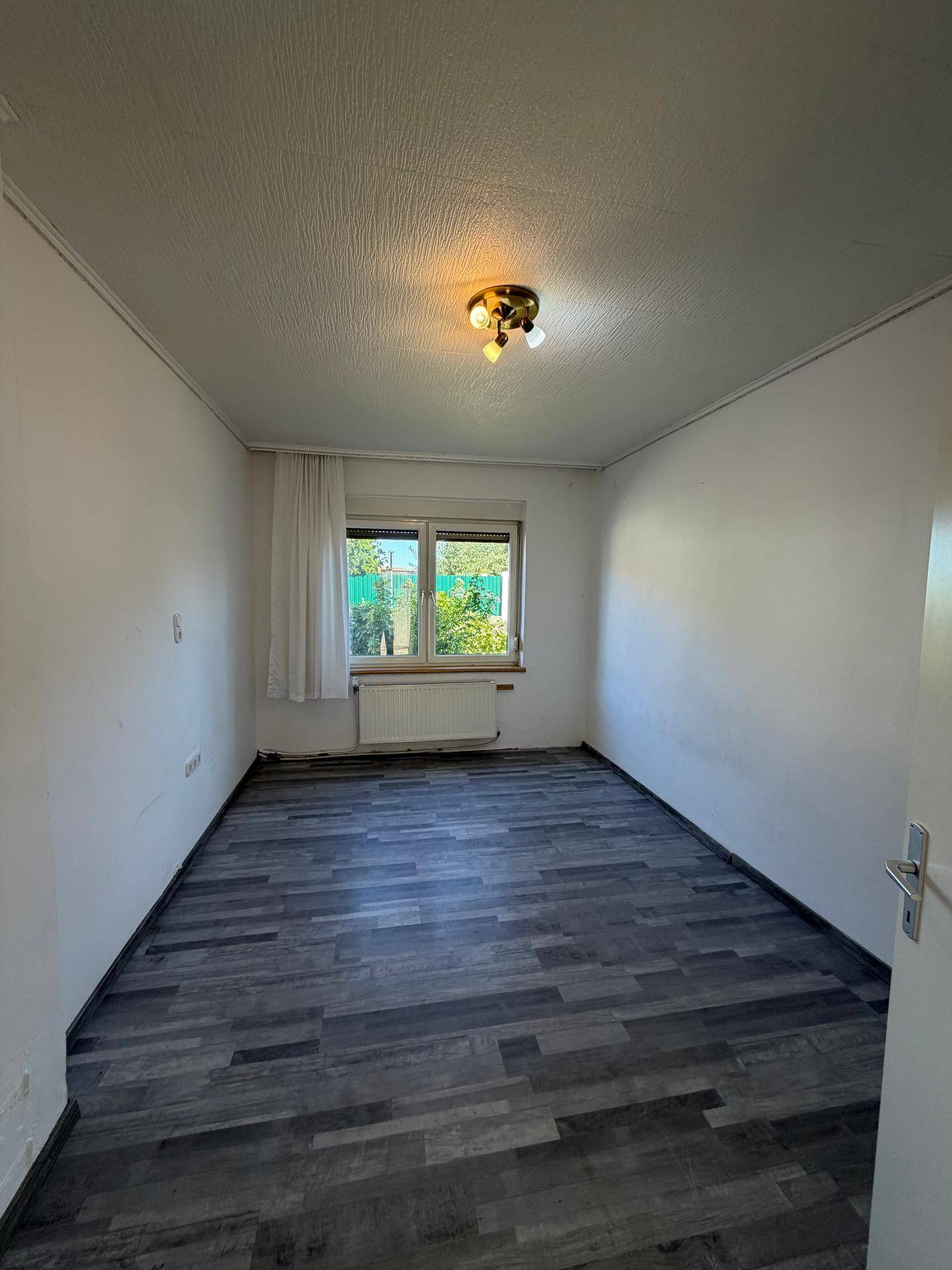 Schlafzimmer mit dunklem Laminatboden und Fenster mit Blick ins Grüne.