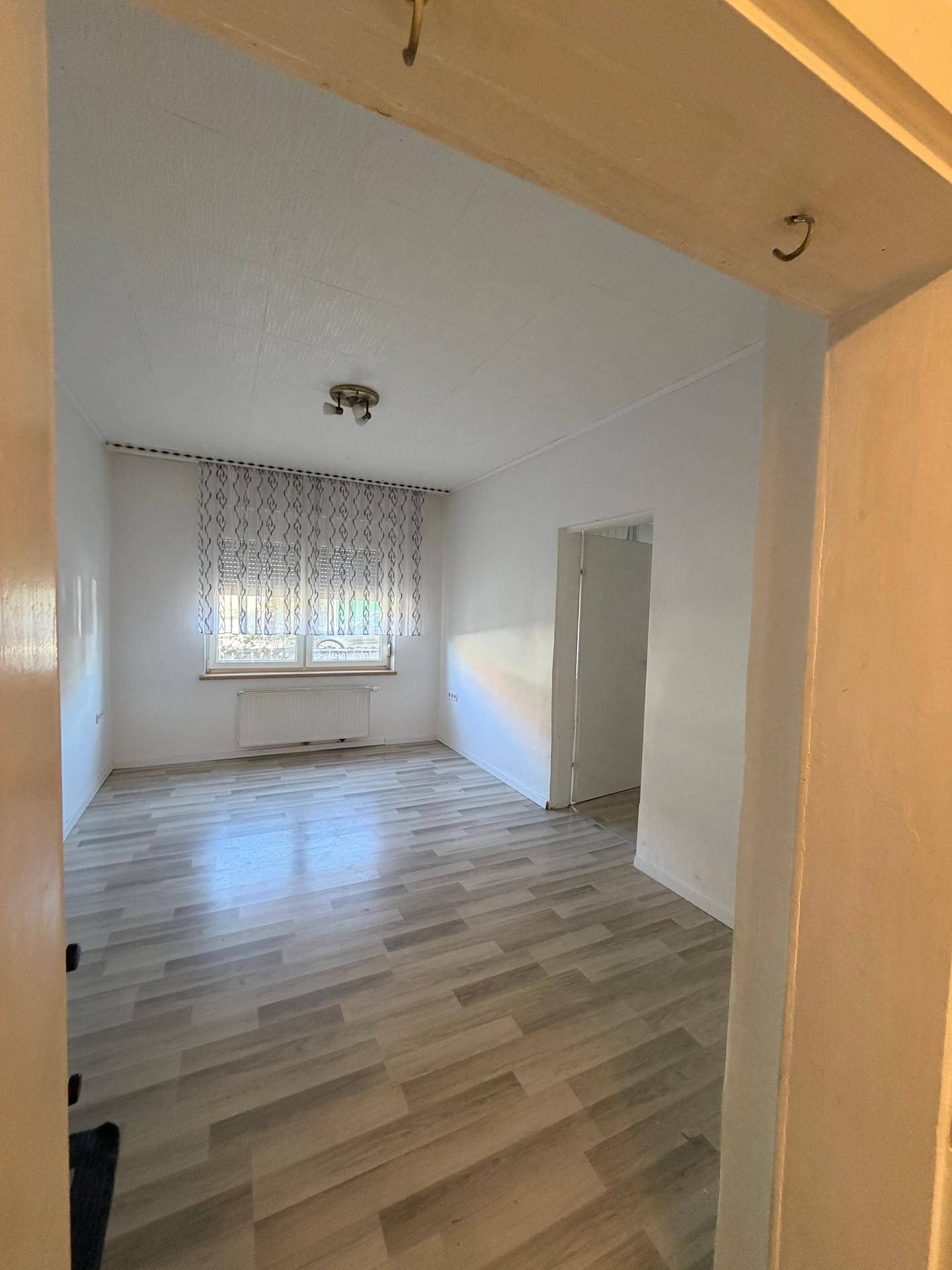 Geräumiges Wohnzimmer mit hellem Laminatboden und viel Tageslicht durch das Fenster.