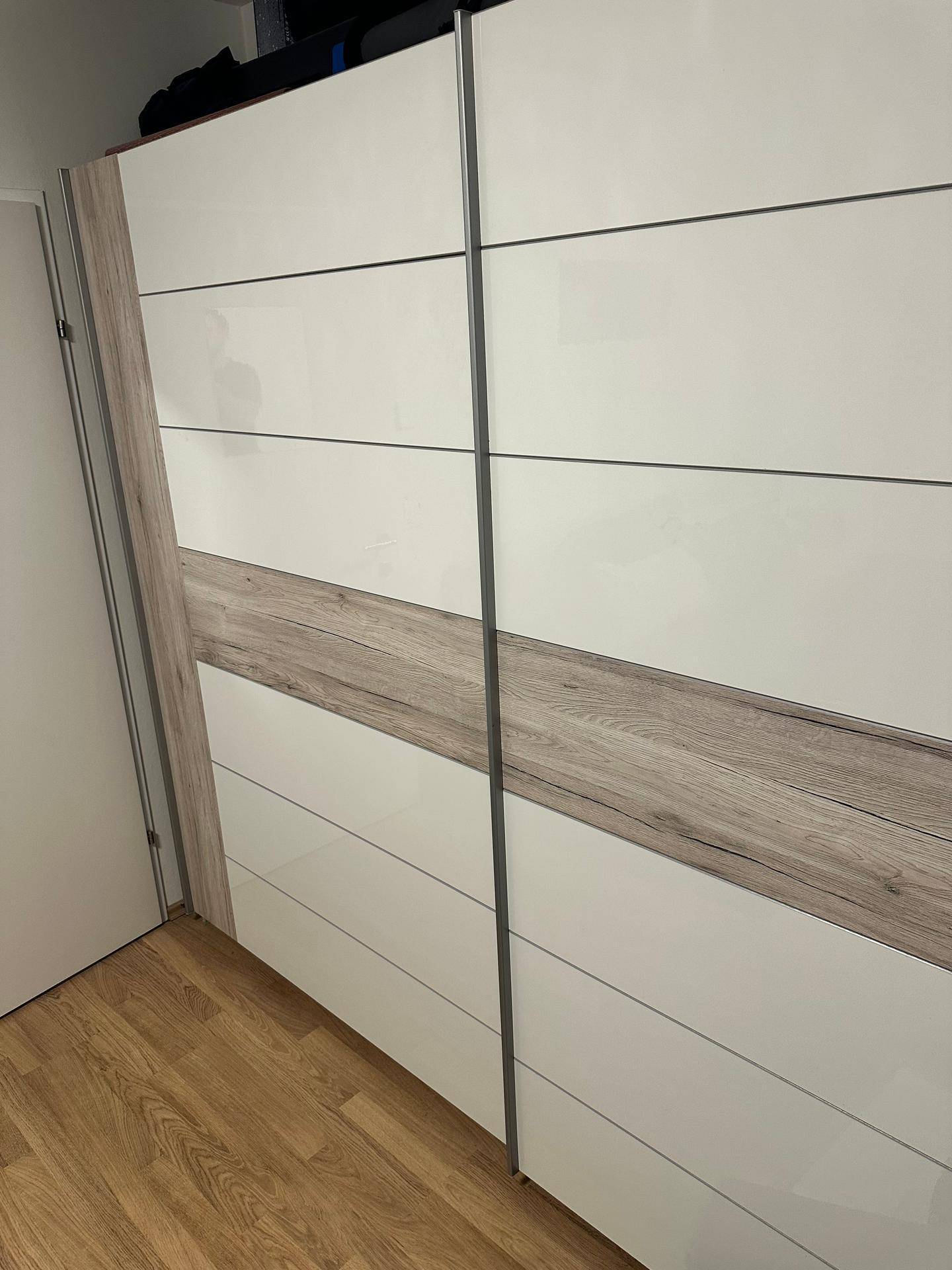 Großer Kleiderschrank mit weißen Hochglanzfronten und Holzakzenten in einem modernen Design.