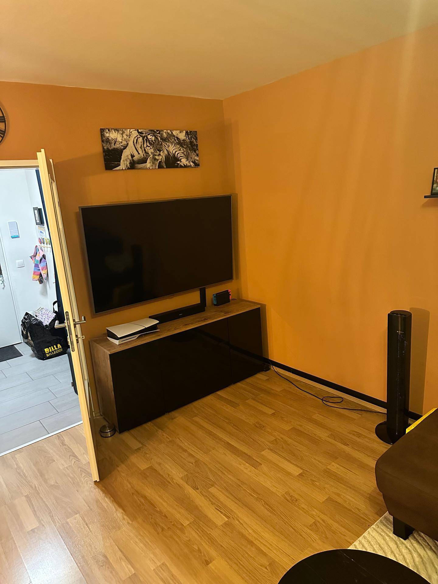 Wohnzimmer mit orangefarbenen Wänden, Laminatboden und einem großen Fernseher auf einem Sideboard.