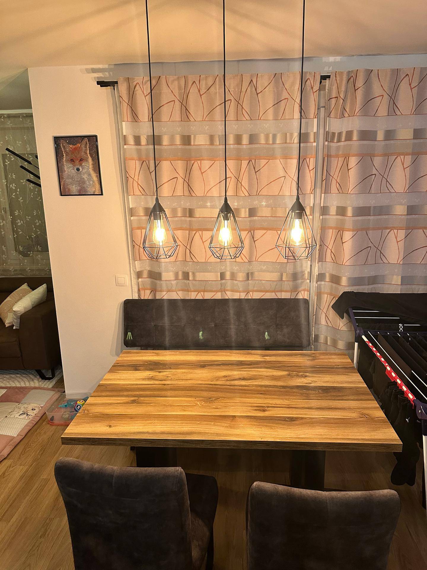 Essbereich mit Holztisch, gepolsterter Sitzbank und modernen Hängelampen über dem Tisch.