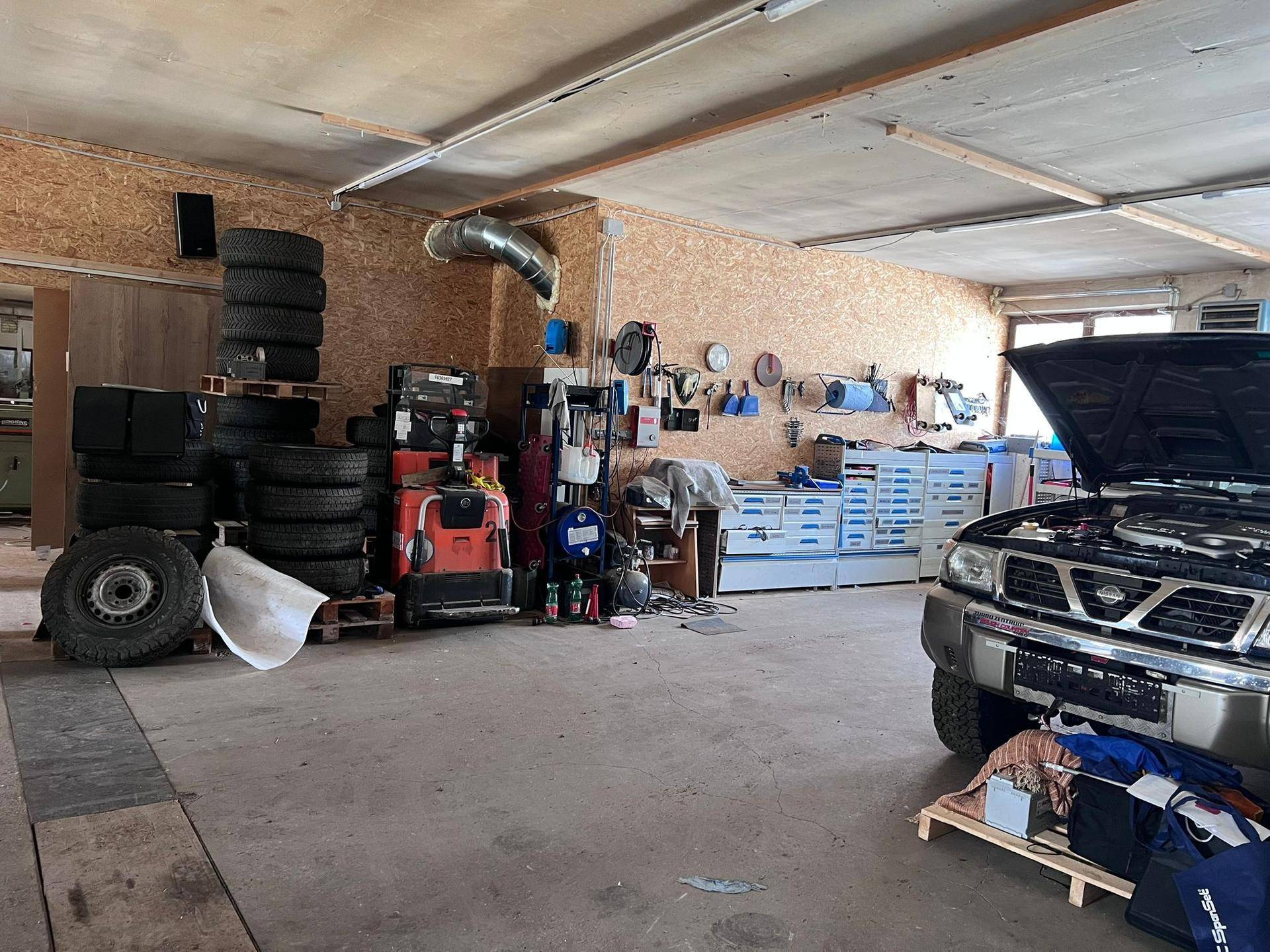 Werkstattbereich in der Garage mit gestapelten Reifen, Werkzeugen und Arbeitsgeräten an den Wänden.