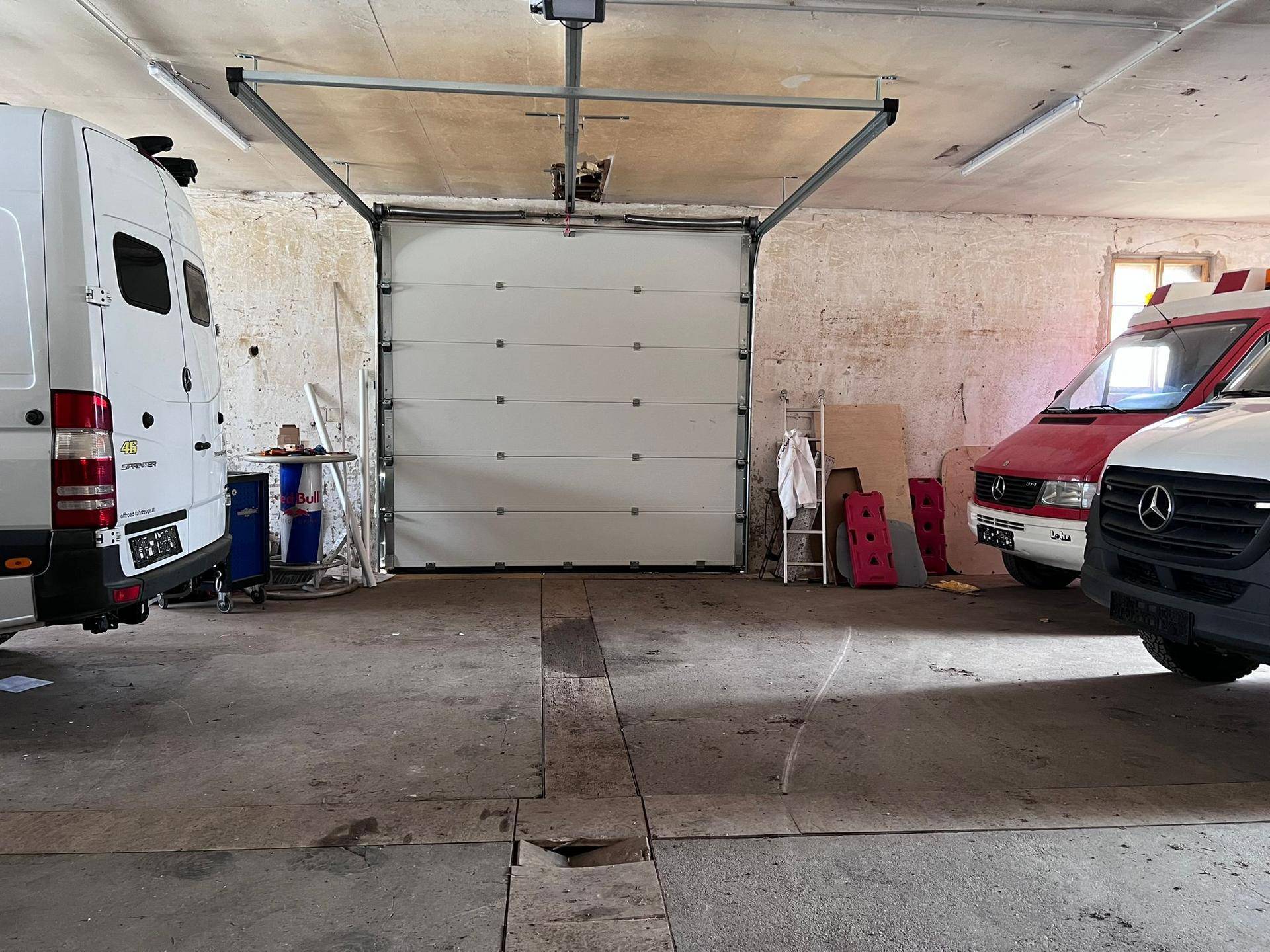Große Garage mit Sektionaltor und Platz für mehrere Fahrzeuge, umgeben von robusten Wänden.