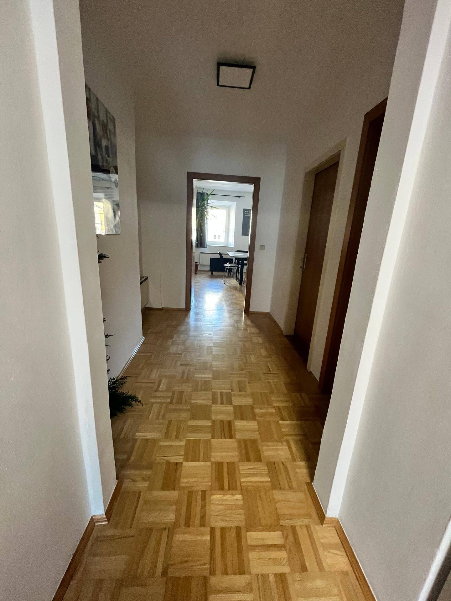 Heller Flur mit Parkettboden, der zu weiteren Räumen und einem Büro führt, gut beleuchtet.
