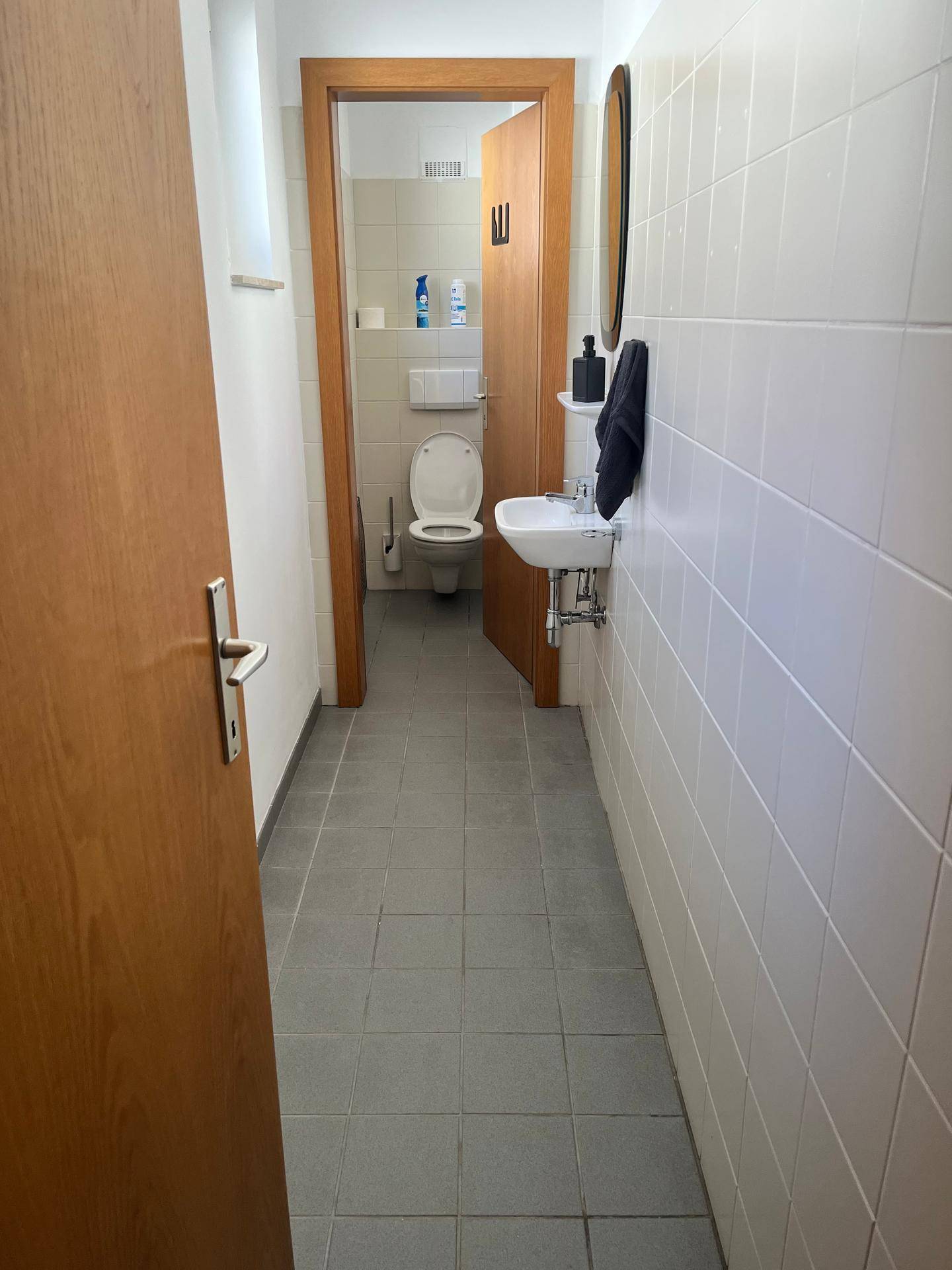 Schmaler Flur führt zu einer Gästetoilette mit weißen Fliesen und kleinem Waschbecken, gut beleuchtet.