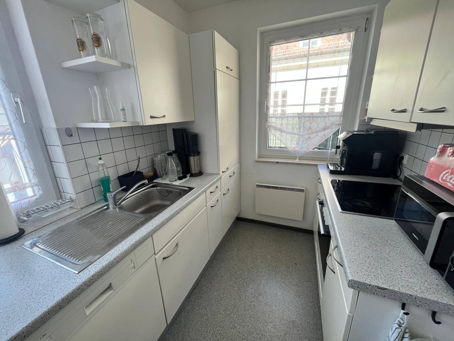 Kleine Küche mit weißen Schränken, Spüle, Kochfeld und einem Fenster mit Blick nach draußen.