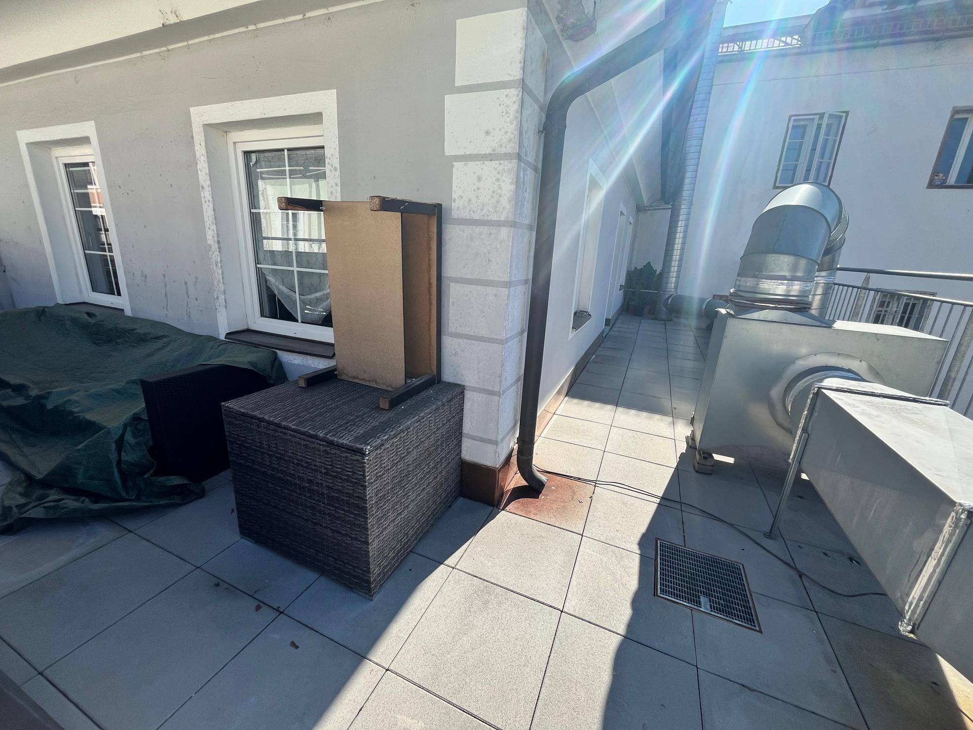 Große Dachterrasse mit Fliesenboden, Gartenmöbeln und Blick auf umliegende Gebäude, sonnig und offen.