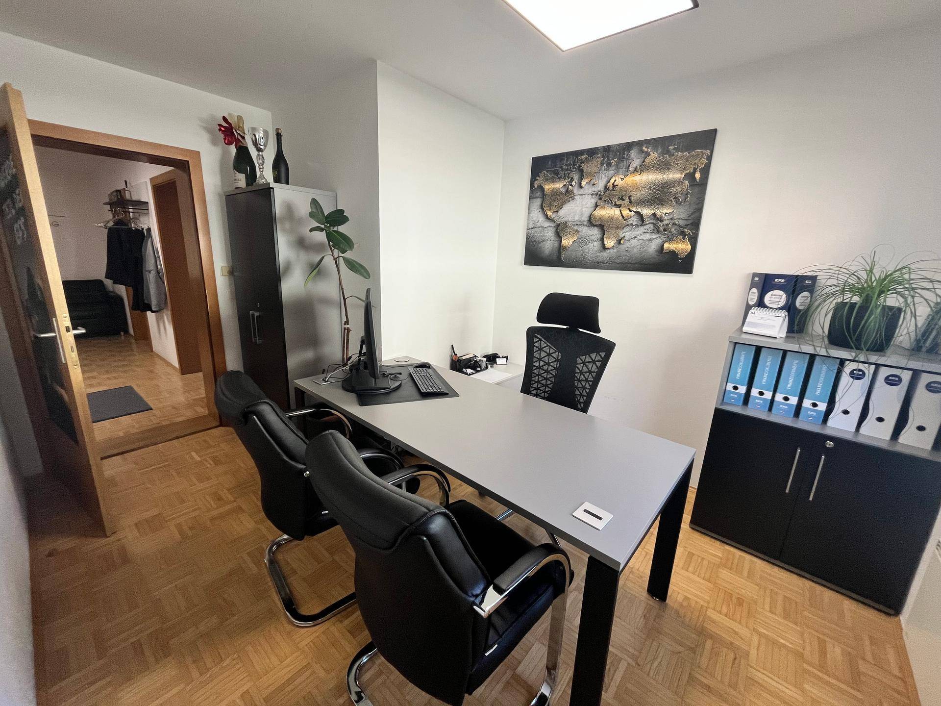 Modernes Büro mit Parkettboden, Schreibtisch, Bürostühlen und einer Weltkarte als Wanddekoration.
