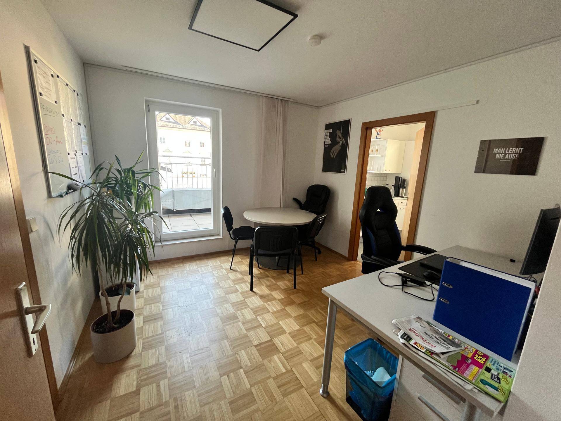 Helles Büro mit Parkettboden, Besprechungstisch, Pflanzen und Zugang zu einem kleinen Balkon.