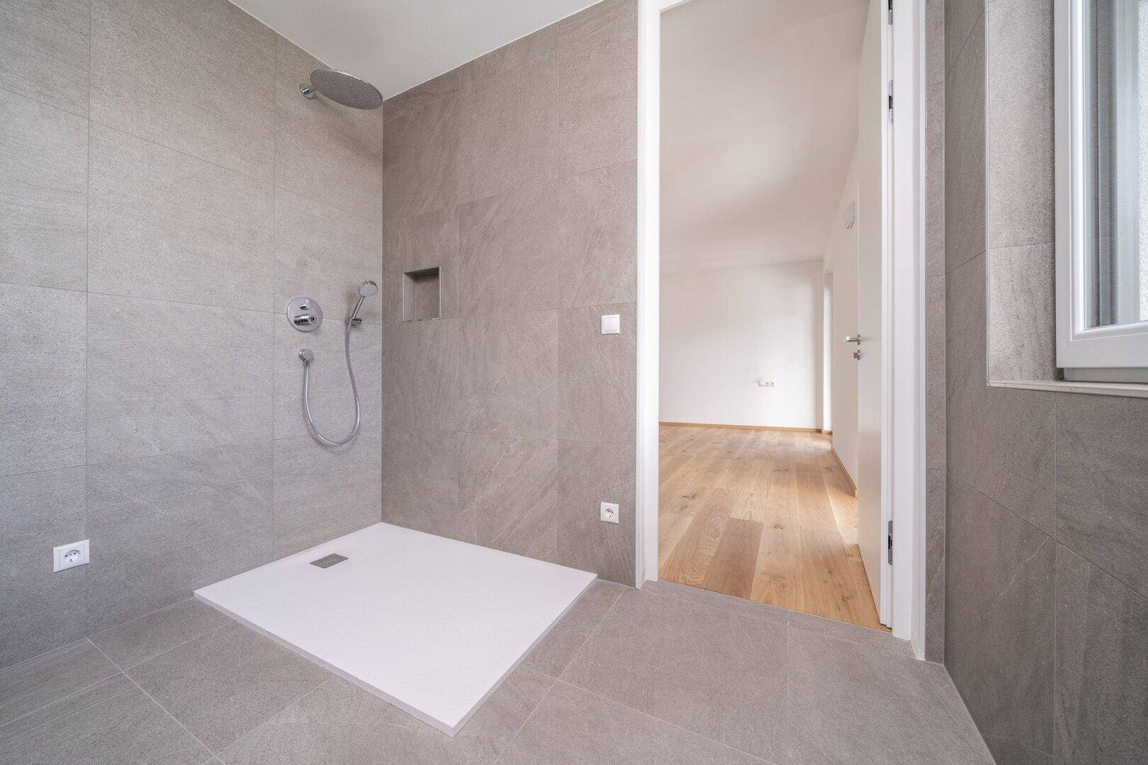 Modernes Badezimmer mit grauen Fliesen, ebenerdiger Dusche und Fenster.