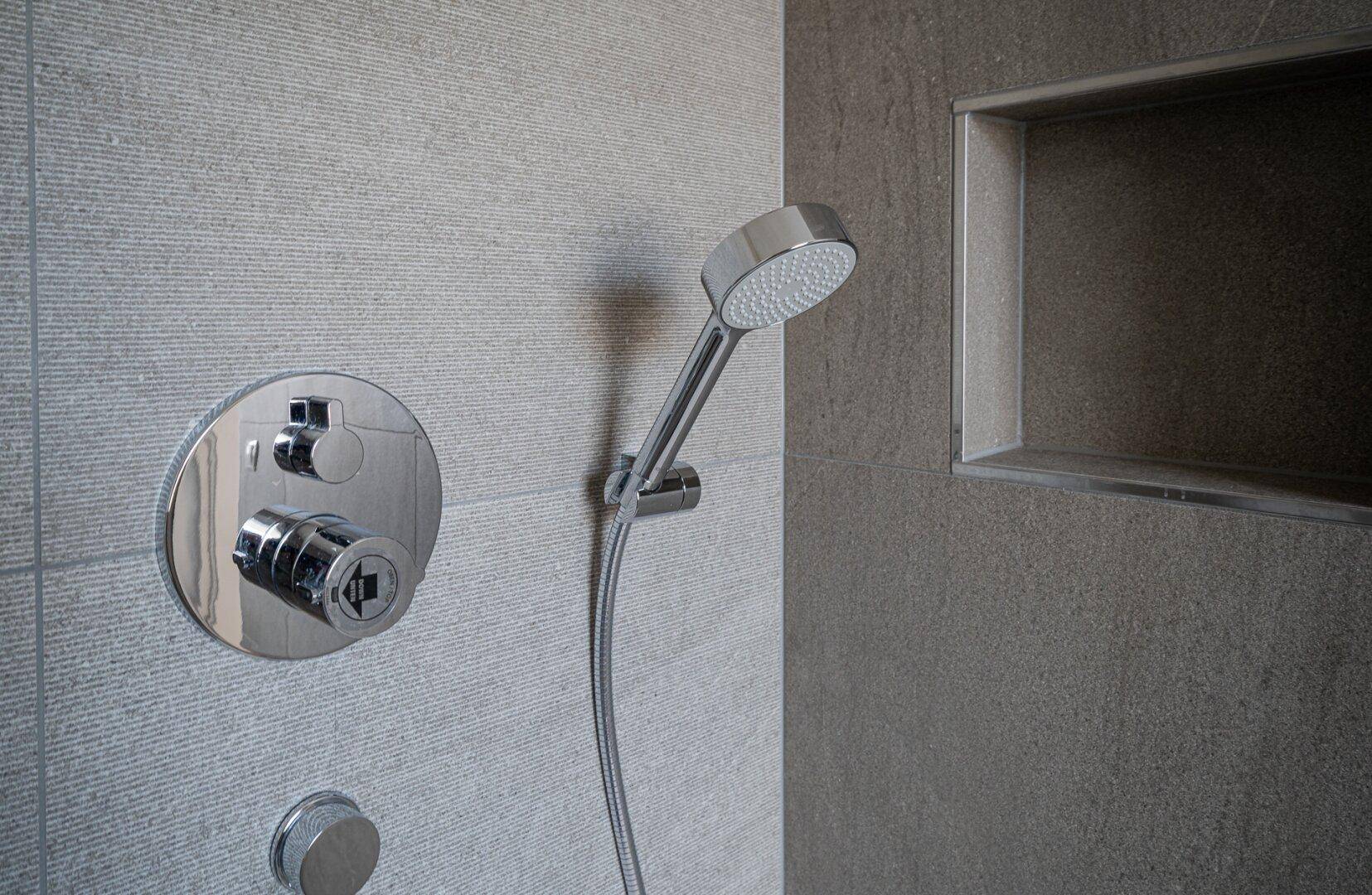 Nahaufnahme der Duscharmatur mit Handbrause und integrierter Nische in einem modernen Badezimmer.