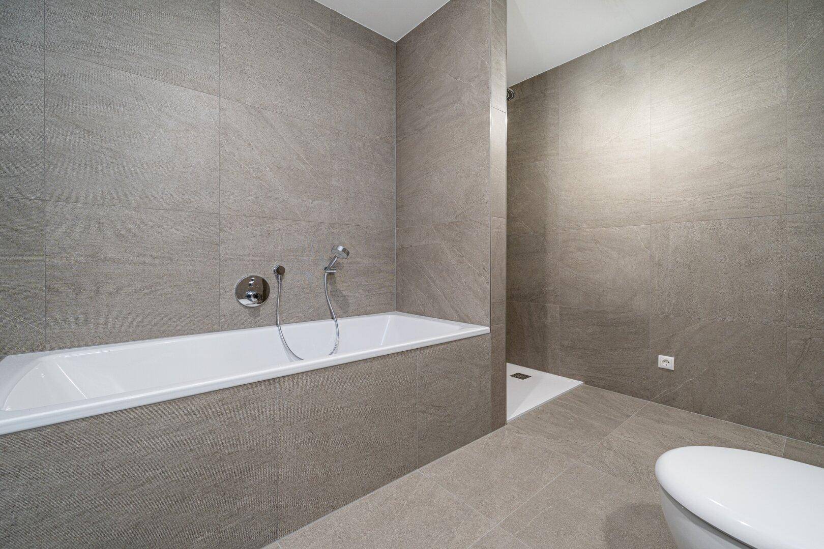 Modernes Badezimmer mit grauen Fliesen, Badewanne und ebenerdiger Dusche.