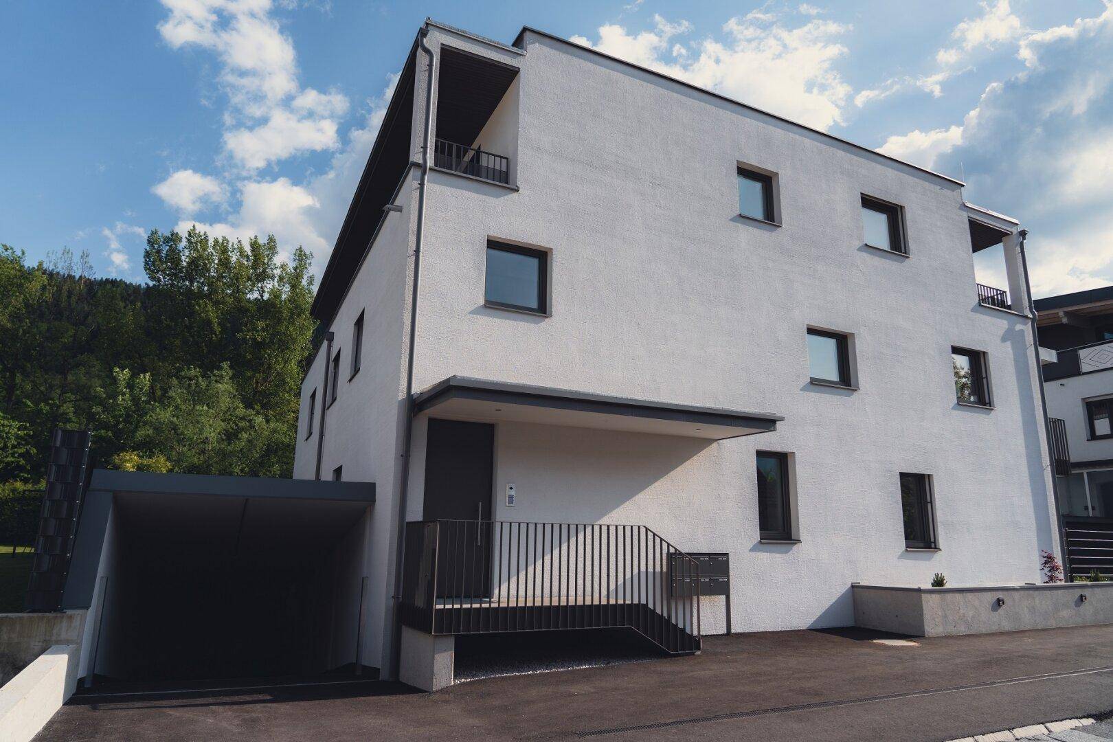 Vorderansicht eines modernen Wohnhauses mit weißer Fassade, Eingangsbereich und integriertem Carport.
