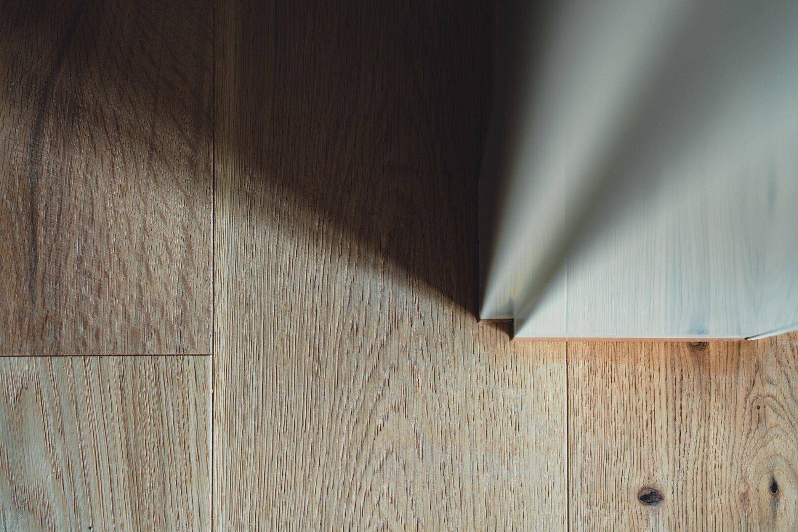 Detailaufnahme eines hellen Holzbodens mit natürlicher Maserung und einem markanten Schattenwurf.