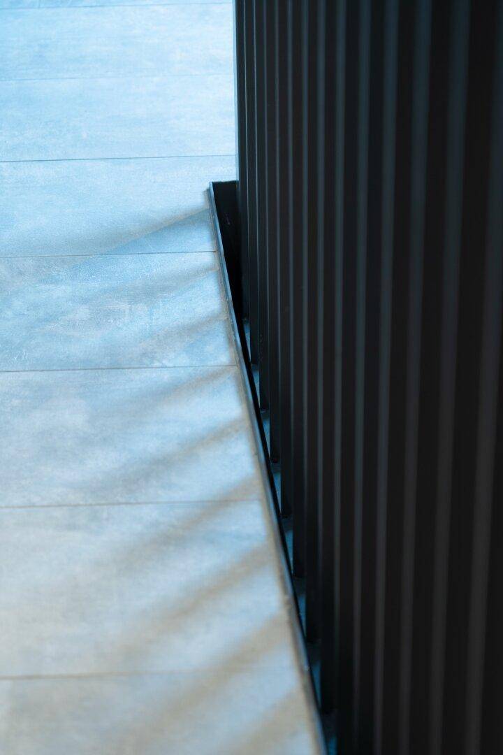 Nahaufnahme eines grauen Fliesenbodens neben einem dunklen, vertikalen Treppengeländer.