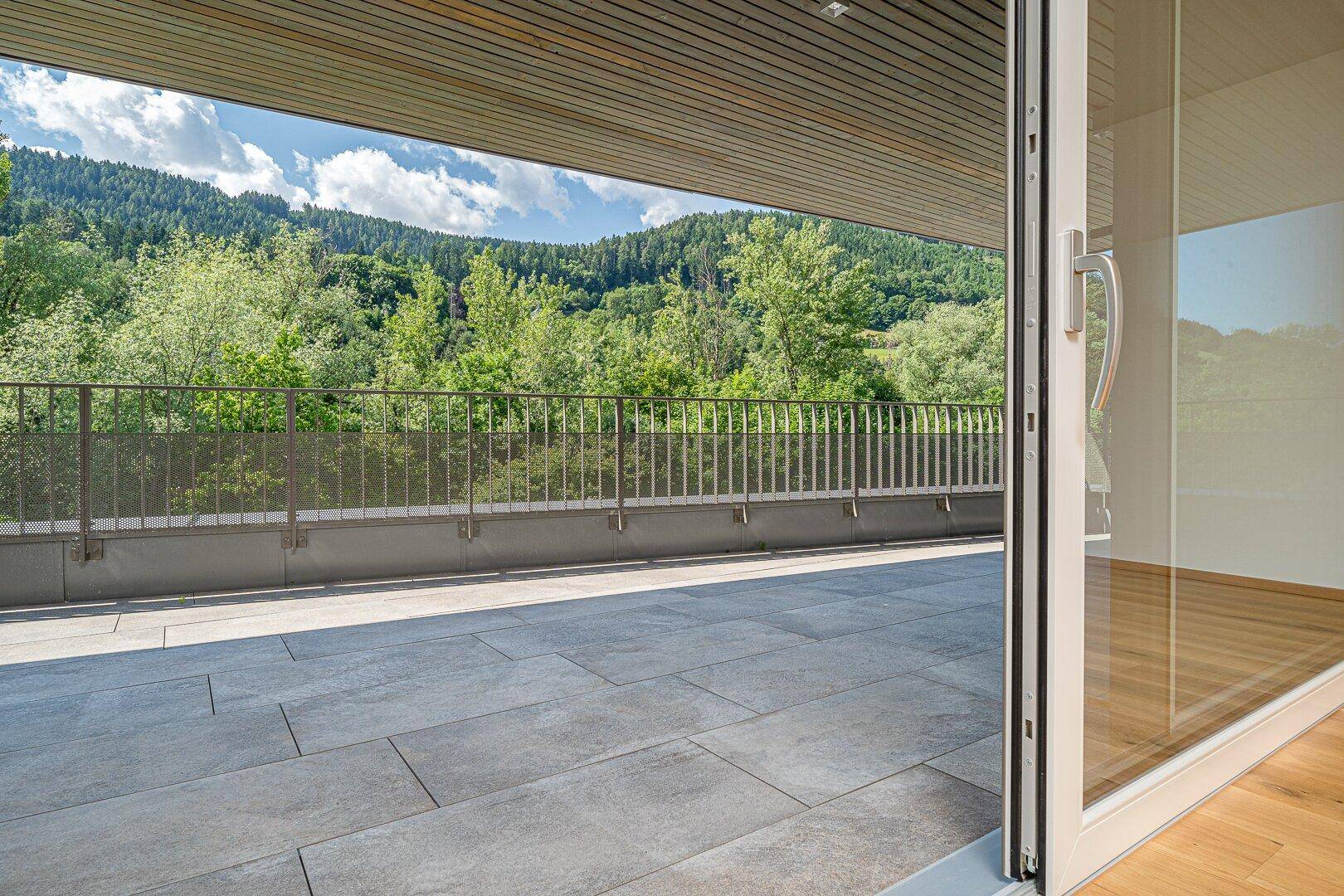 Geräumige Terrasse mit Fliesenboden und weitem Blick auf die grüne Berglandschaft.